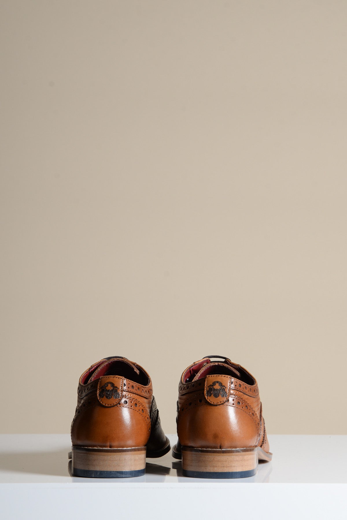 The marcdarcy BRANDON Dark Tan Leather Wingtip Brogue Shoes, featuring hand-stitched detailing and decorative perforations, are shown from the back on a white surface with a beige background.