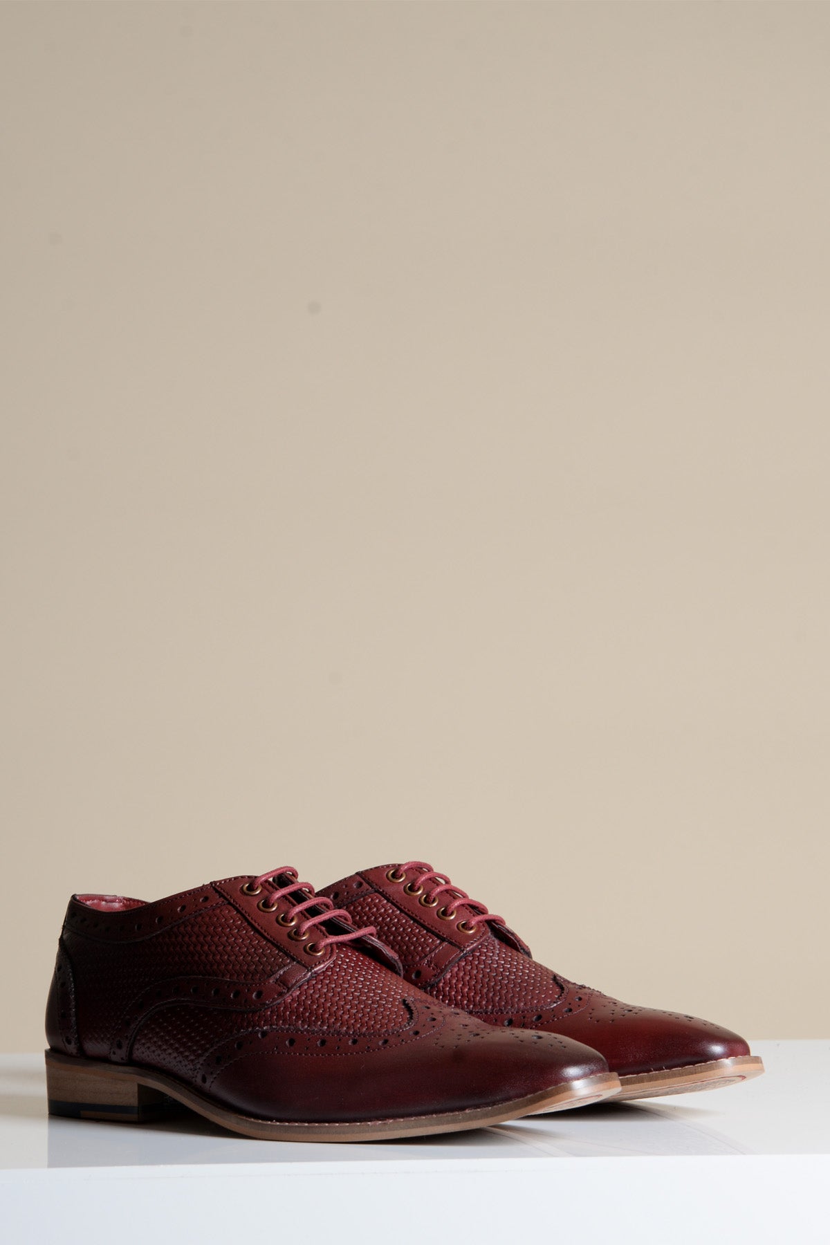 The marcdarcy BRANDON Bordeaux Burgundy Leather Wingtip Brogue Shoes feature hand-crafted detailing and laces, showcased on a white surface with a beige background.