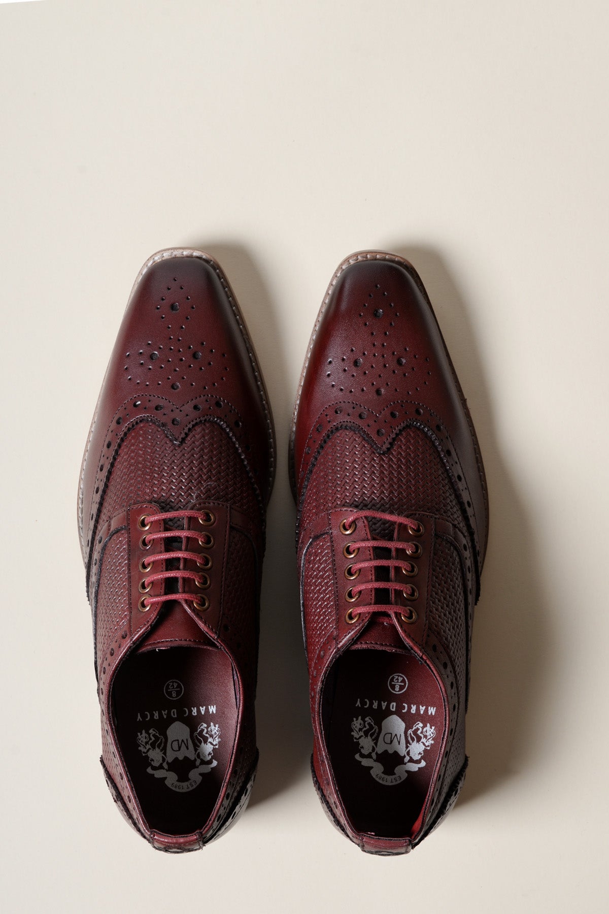 The marcdarcy BRANDON Bordeaux Burgundy Leather Wingtip Brogue Shoe features red laces and textured full grain leather, hand-stitched and shown flat on a cream background in a top-down view.