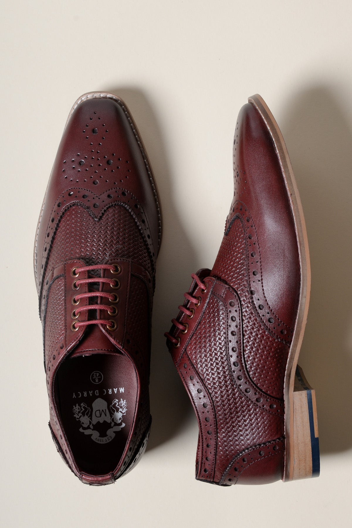 The marcdarcy BRANDON is a bordeaux burgundy leather wingtip brogue shoe featuring detailed perforations and woven texture, shown on a light surface with one shoe viewed from above and the other from the side—premium men's footwear.
