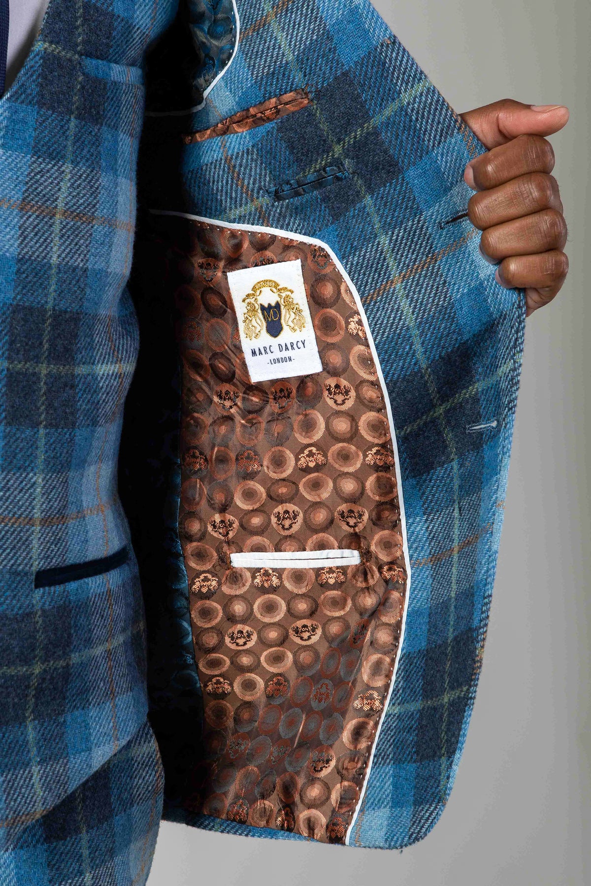 Close-up of a man's hand holding the lapel of the Marc Darcy MORRIS Blue Tweed Check Blazer, featuring a brown circular-patterned lining and the Marc Darcy label.