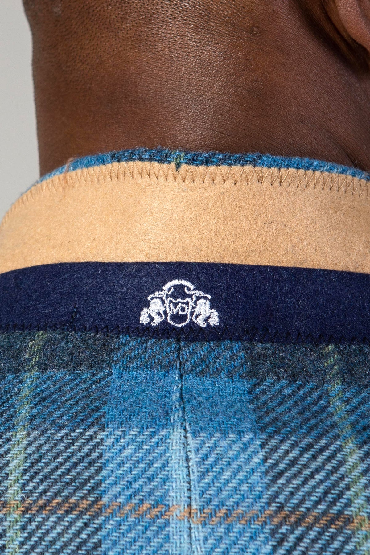 A close-up of a person's neck wearing the Marc Darcy MORRIS - Blue Tweed Check Blazer, featuring a tan wool collar with a navy band and a white embroidered crest.