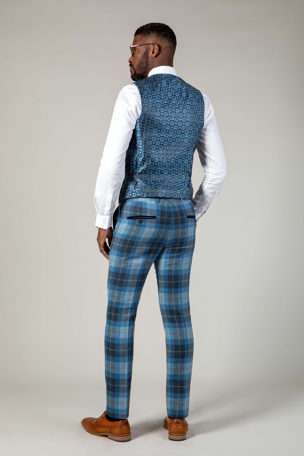 Back view of a man wearing the Marc Darcy MORRIS - Blue Tweed Check Waistcoat, styled with a white dress shirt, blue plaid pants, and brown dress shoes for a modern tailored look.