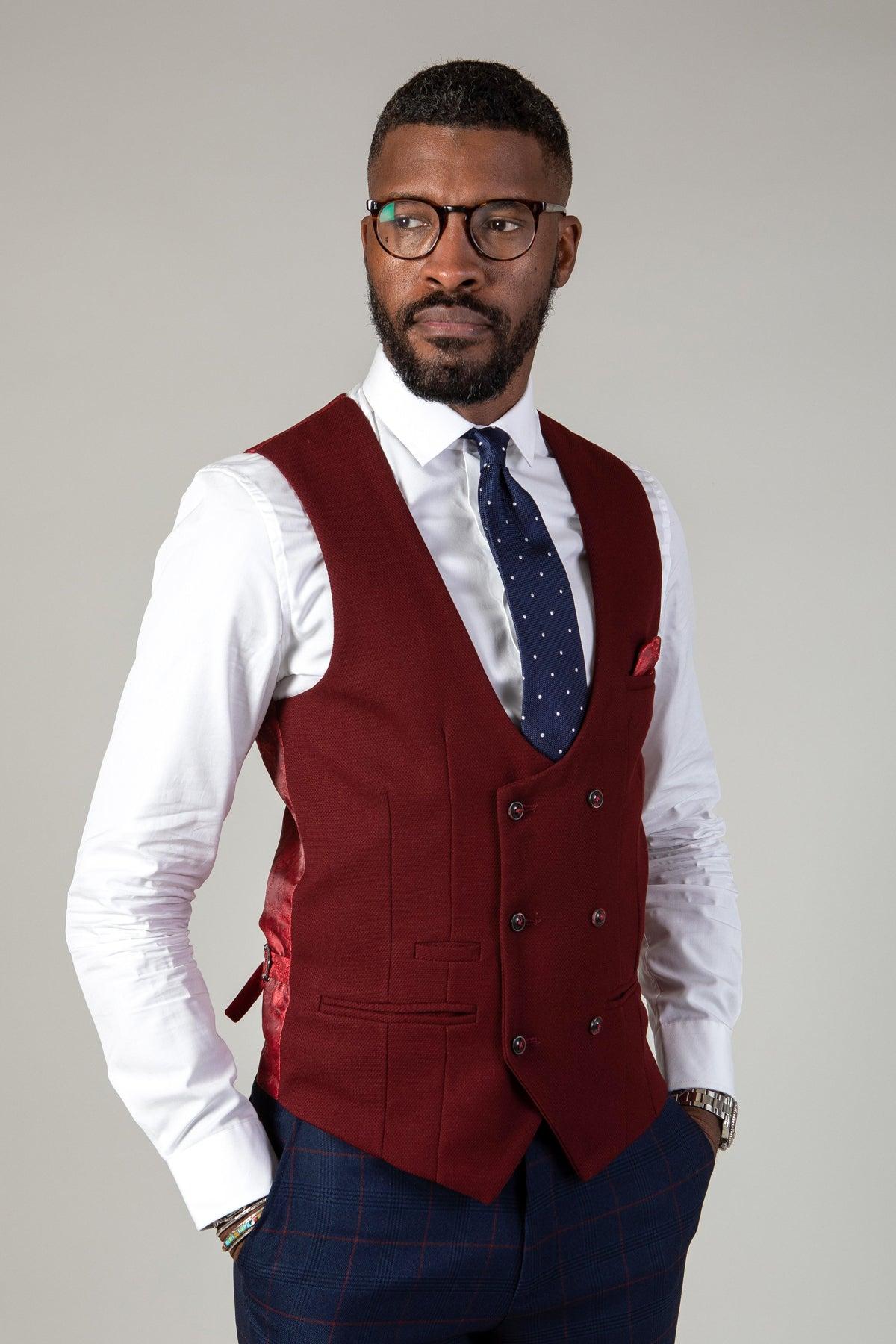 A man in glasses, white dress shirt, navy polka-dot tie, and the marcdarcy KELVIN Wine Double Breasted Waistcoat with matching pocket square stands with hands in pockets against a plain background.