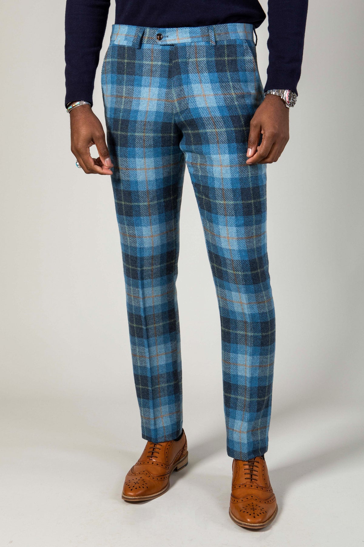 Wearing Marc Darcys MORRIS Blue Tweed Check Trousers, a dark long-sleeve shirt, brown leather brogue shoes, and a watch, the person stands against a plain light background with their head not visible in the image.