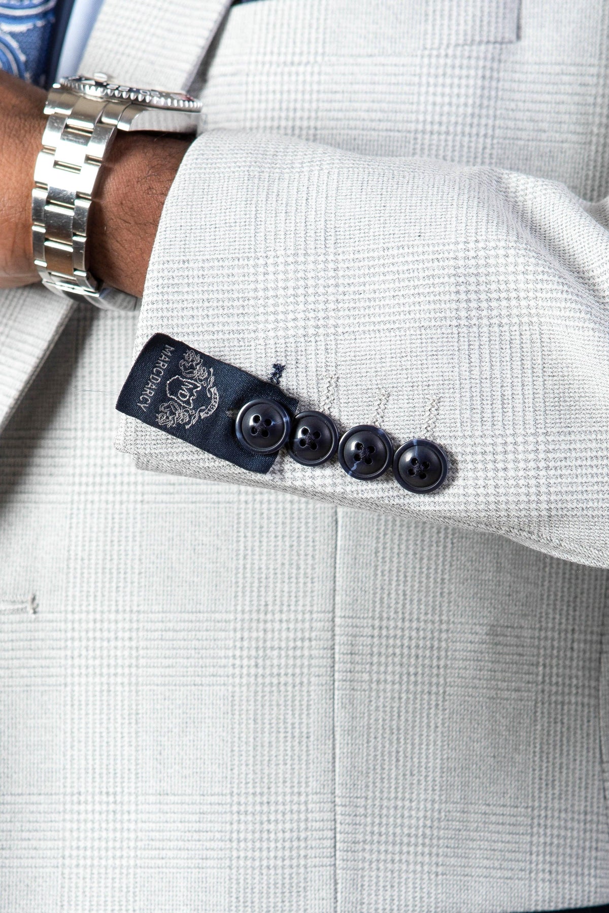 A close-up of a person’s arm in a slim fit stone check Marc Darcy BROMLEY suit jacket with four black cuff buttons, visible designer label, and a silver wristwatch, styled with the Kelvin Pink Waistcoat.