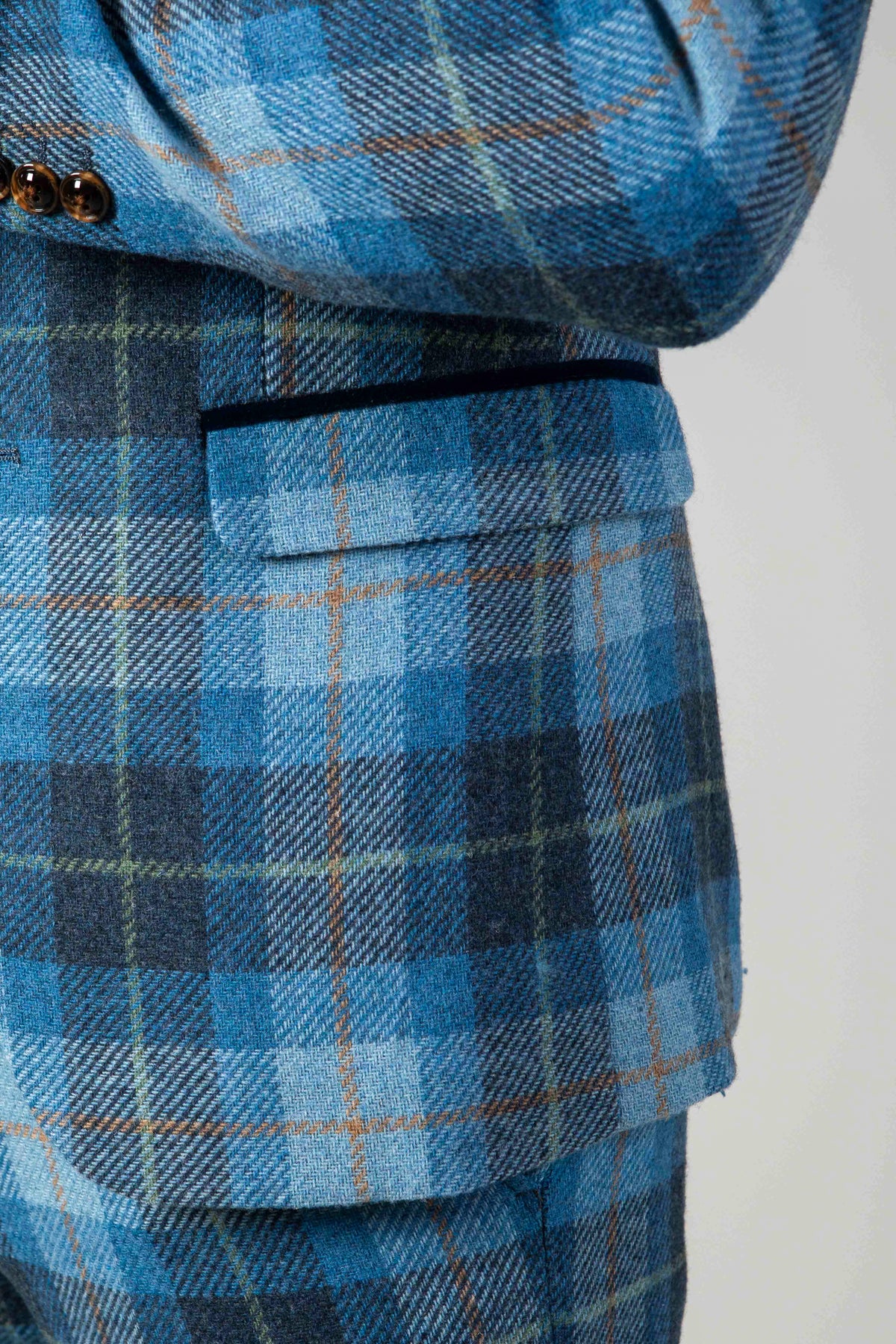 Close-up of a person in the Marc Darcy MORRIS Blue Tweed Check Blazer, featuring a blue windowpane check pattern with shades of blue, gray, and a hint of orange, brown buttons, and a front pocket.