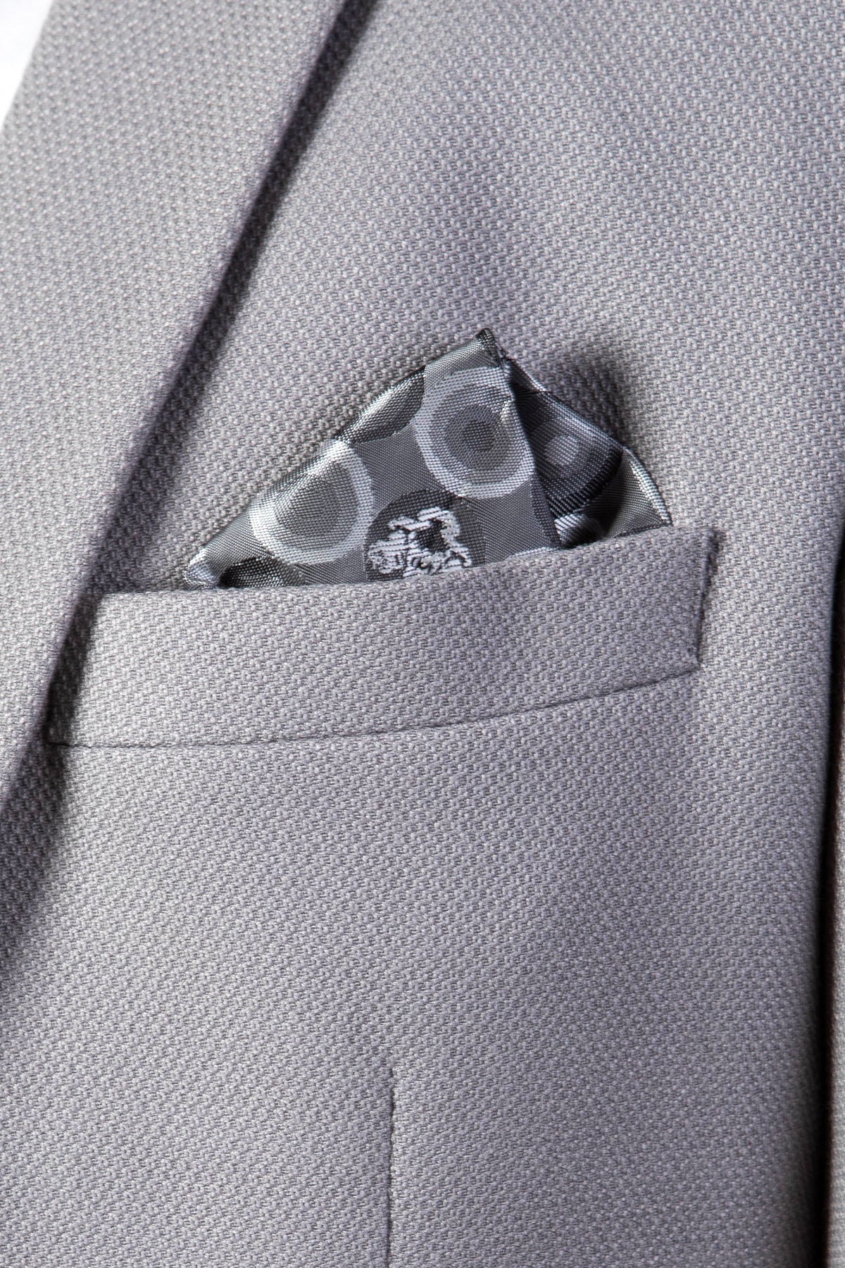 A close-up of the marcdarcy EDWIN Silver Grey Notch Lapel Two Piece Suit jacket pocket, showcasing a neatly folded patterned silk pocket square with circular designs.