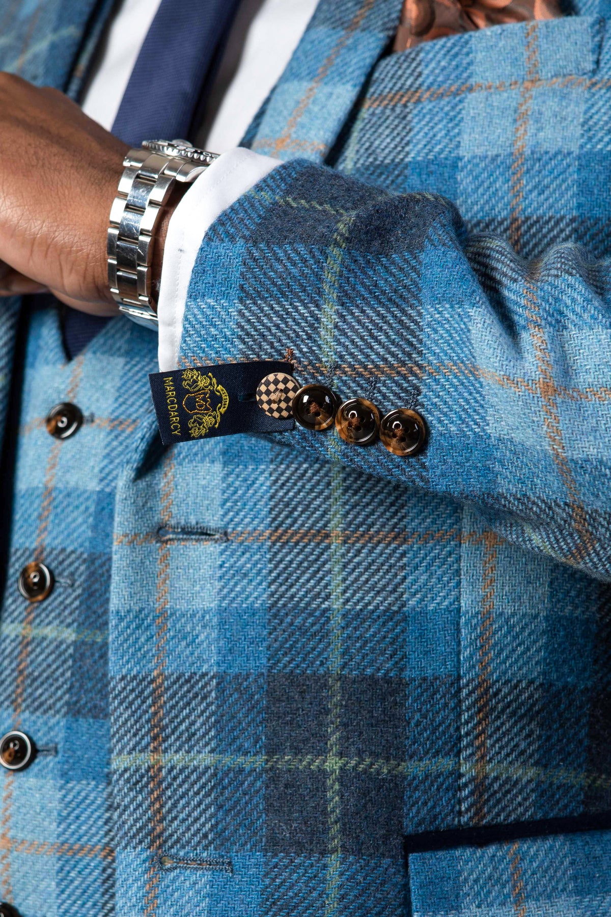 Close-up of a man's arm in the blue tweed check MORRIS blazer by Marc Darcy, featuring brown buttons, a silver watch, and a visible cuff tag highlighting this stylish slim fit blazer.