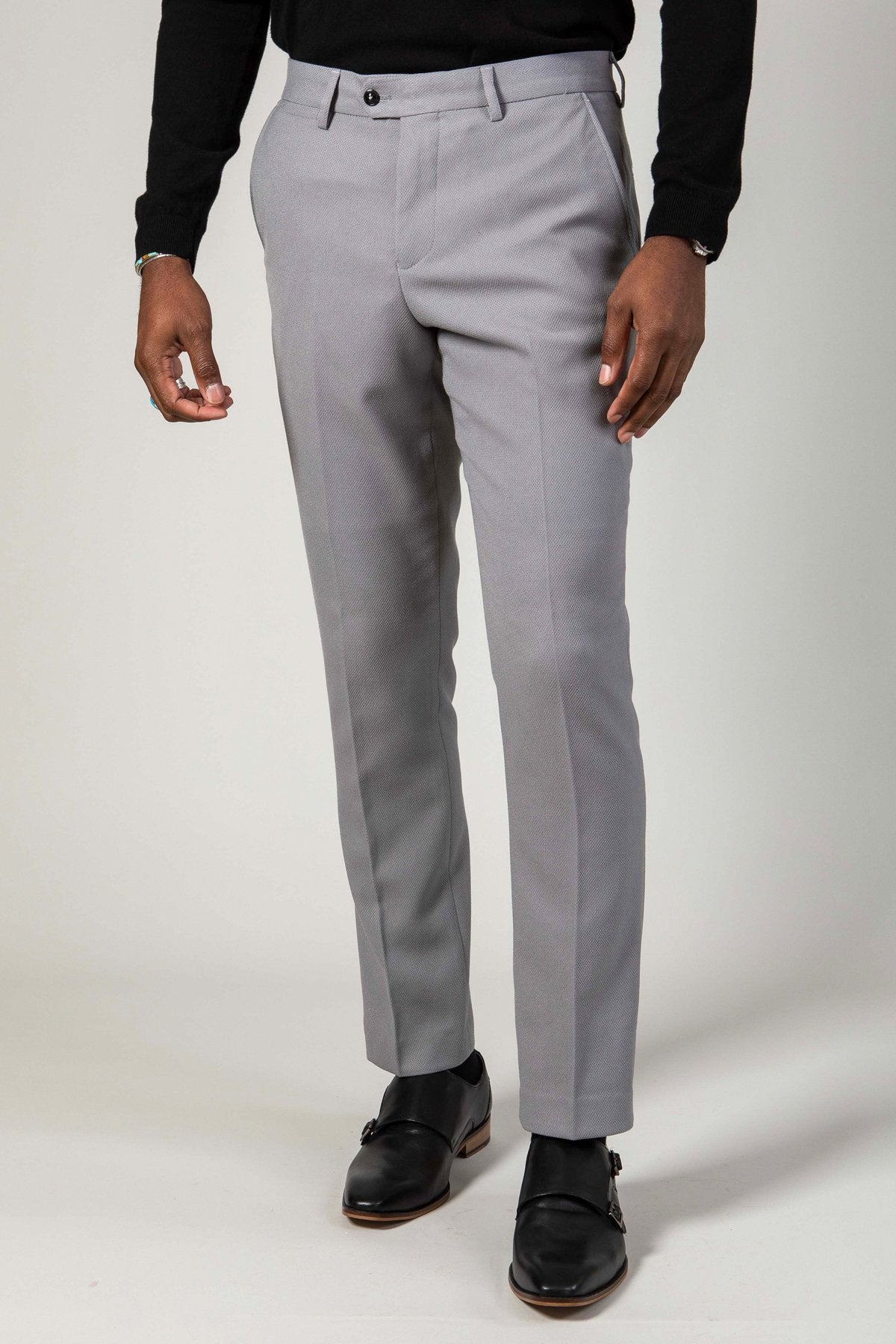 A person models the lower half of the marcdarcy EDWIN - Silver Grey Notch Lapel Three Piece Suit pants with a black long-sleeve shirt and black dress shoes, standing against a plain light background.