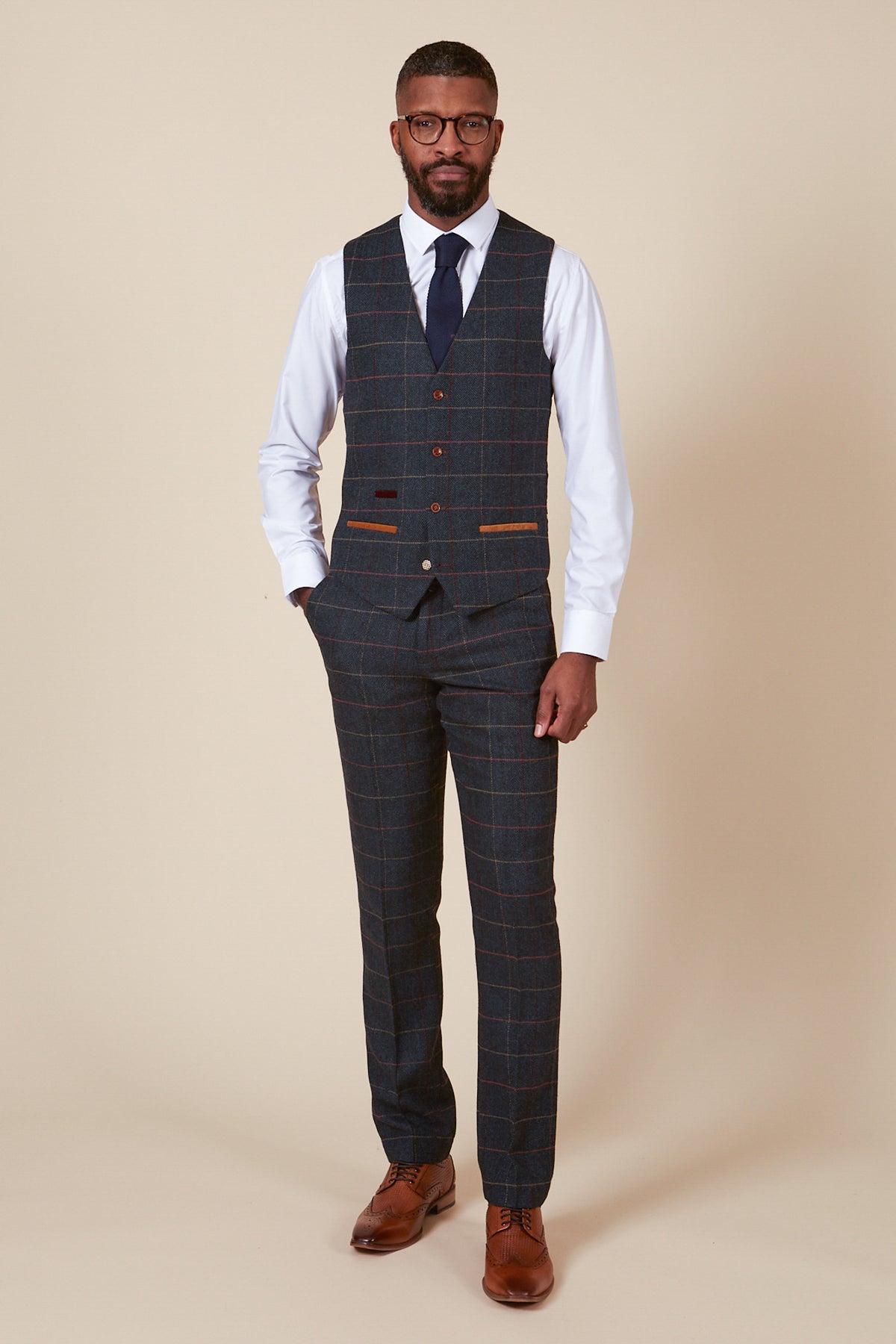 A man stands against a cream background wearing marcdarcy’s ETON Single Breasted Navy Blue Tweed Check Waistcoat—an ideal look for countryside wedding wear.