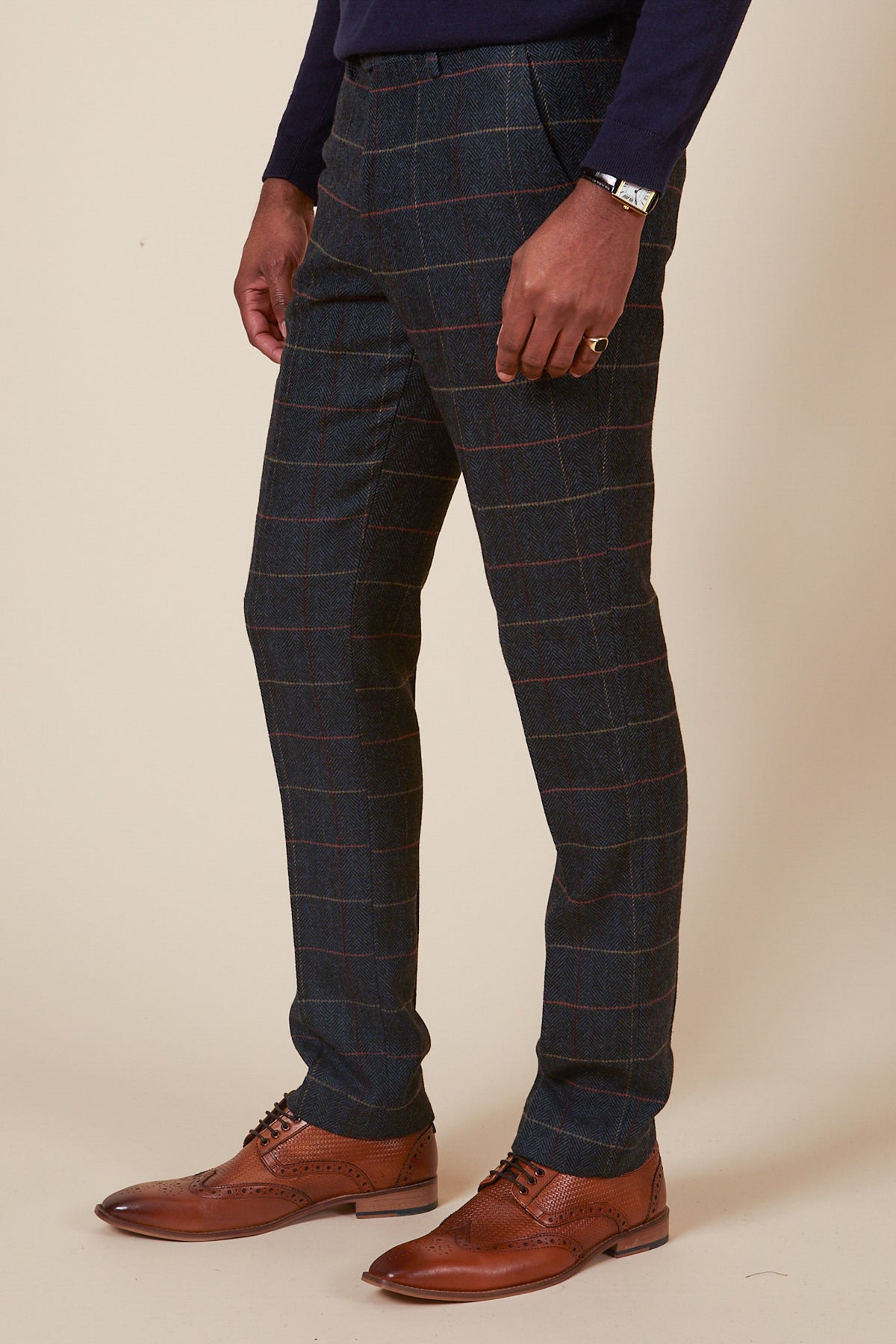 Someone wearing marcdarcy ETON Navy Blue Tweed Check Trousers, a navy long-sleeve shirt, a bracelet, and brown leather dress shoes stands against a plain beige background.