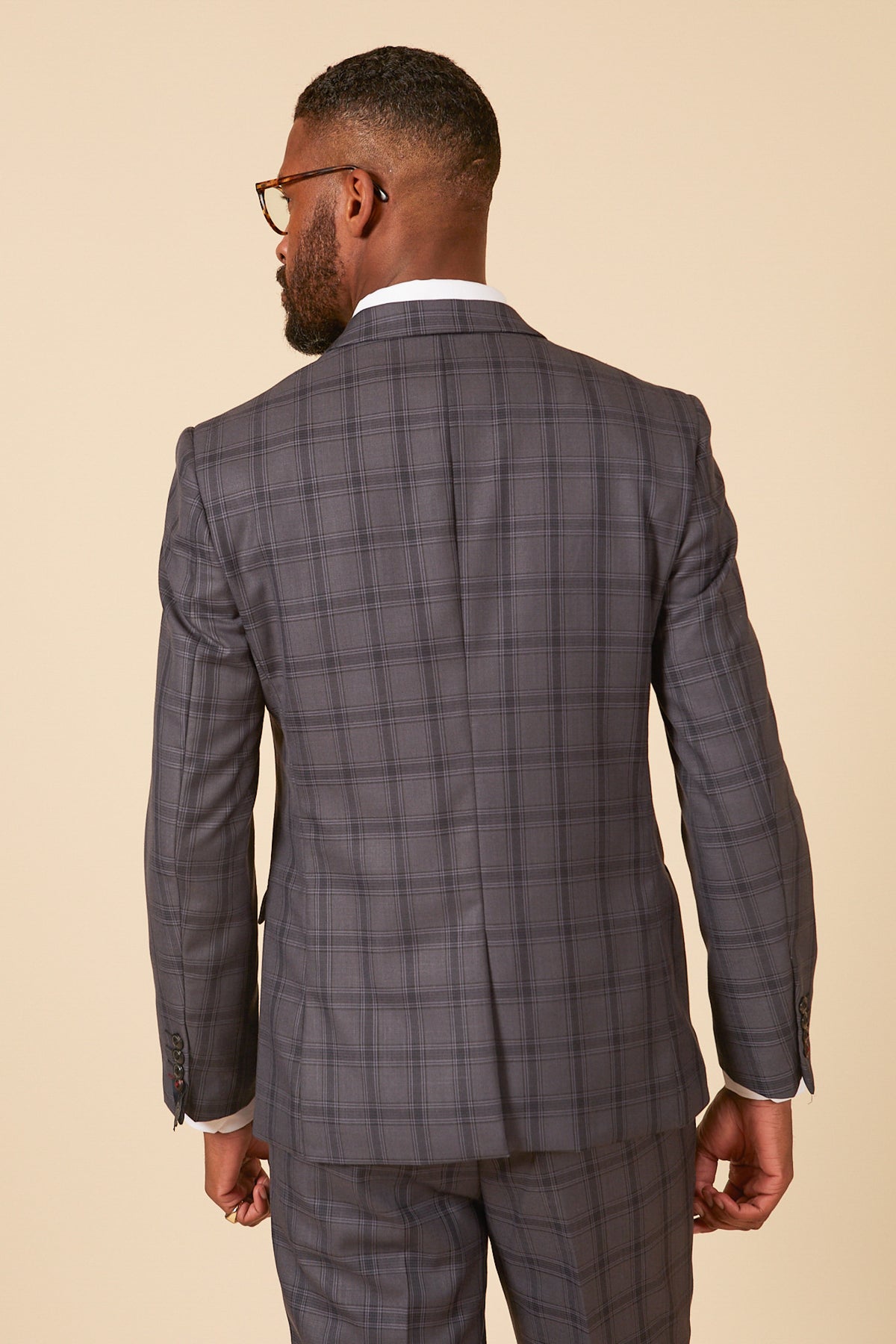 A man wearing glasses and the Marc Darcy JOSE Grey Check Blazer is seen from behind against a beige background.