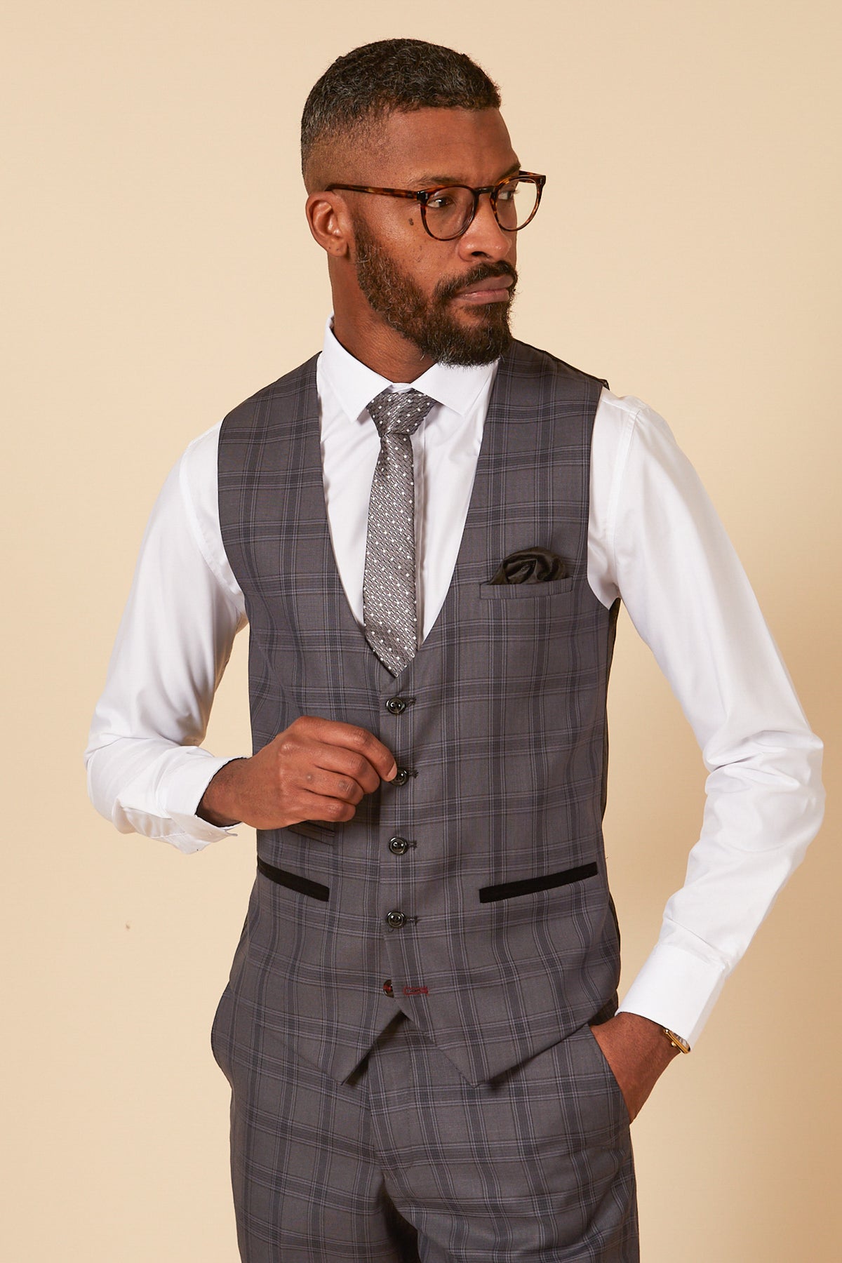 A man with glasses and a beard looks to his right, dressed in a marcdarcy JOSE Grey Check Single Breasted Waistcoat, white shirt, and patterned tie.