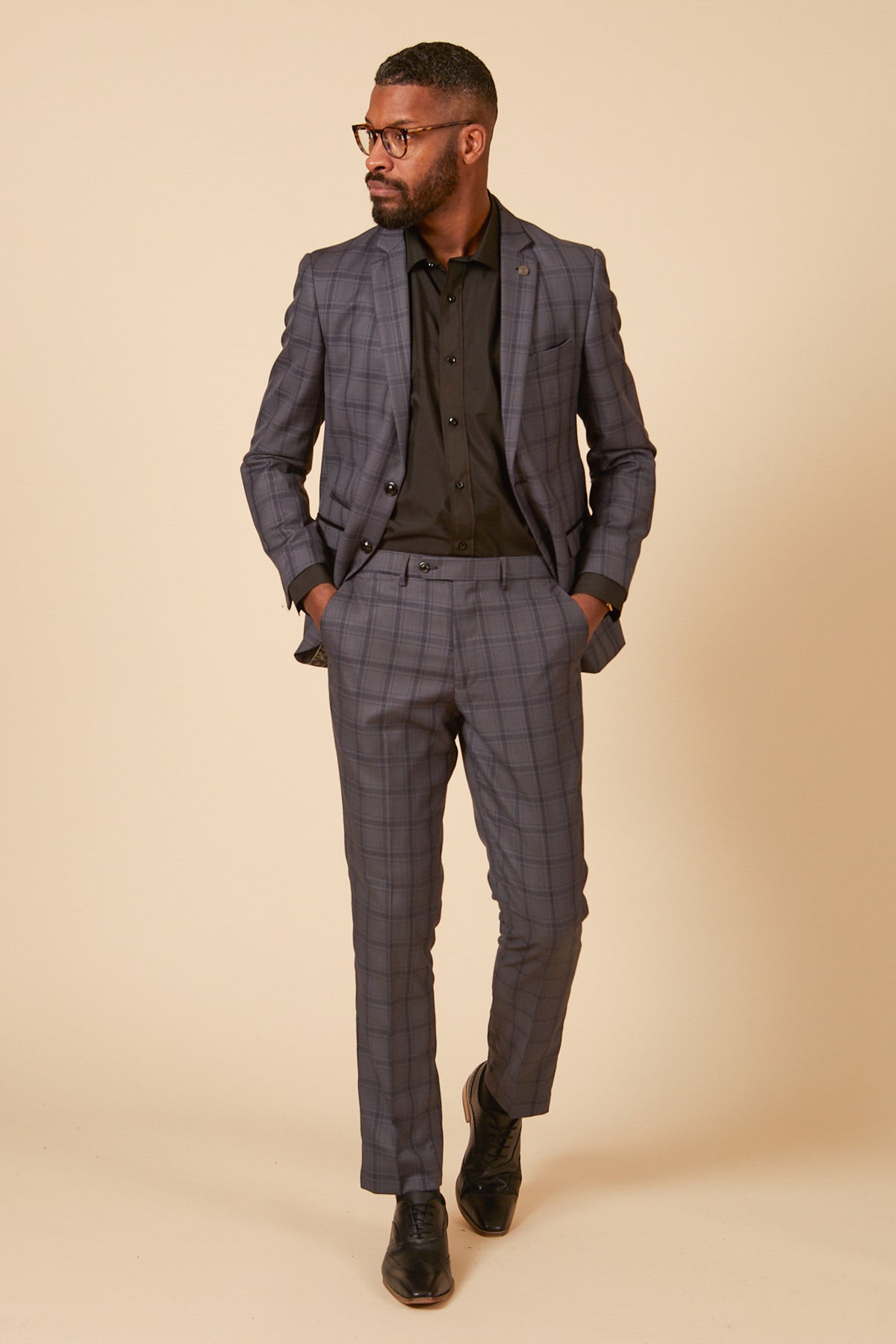 A man in the Marc Darcy JOSE Grey Check Blazer with a tailored fit stands with hands in his pockets, looking to the side against a plain beige background.