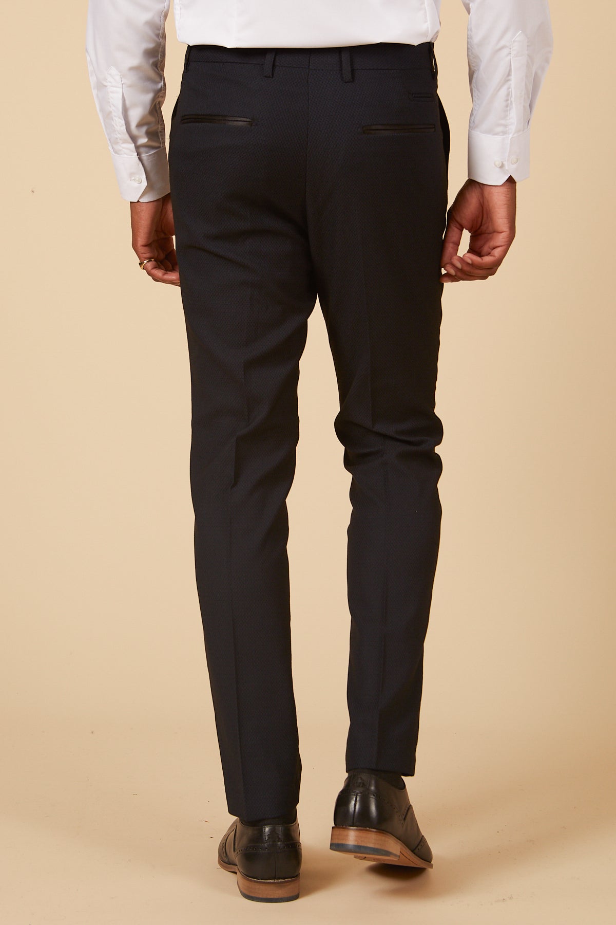 A man is seen from behind wearing a white shirt and marcdarcy's DALTON Navy Diamond Trousers, paired with black dress shoes, standing against a beige background.