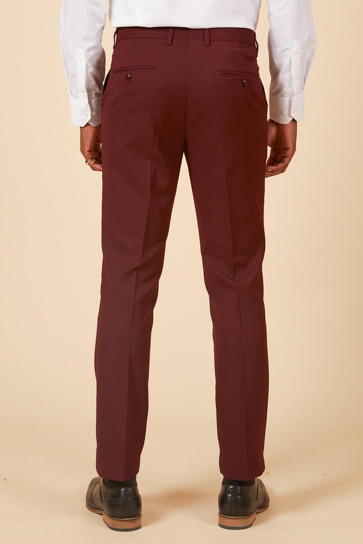 A man, seen from the back, wears marcdarcys MAX - Wine Three Piece Suit pants in diamond-textured fabric with a white shirt and brown dress shoes against a beige background; only his lower back and legs are visible.