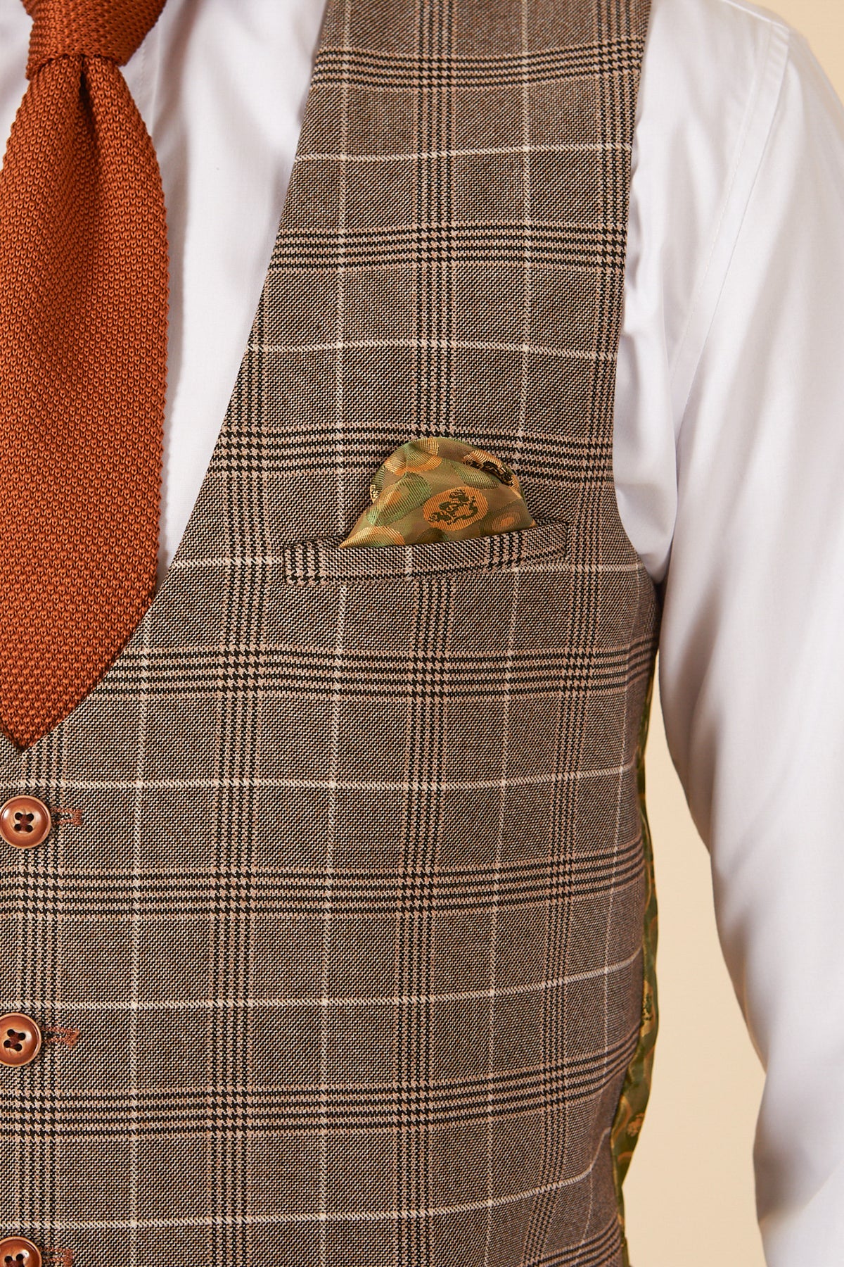A person wearing a white shirt, an orange textured tie, and the marcdarcy RAY - Tan Check Waistcoat with brown buttons and a patterned pocket square. Image is cropped to show only the torso.