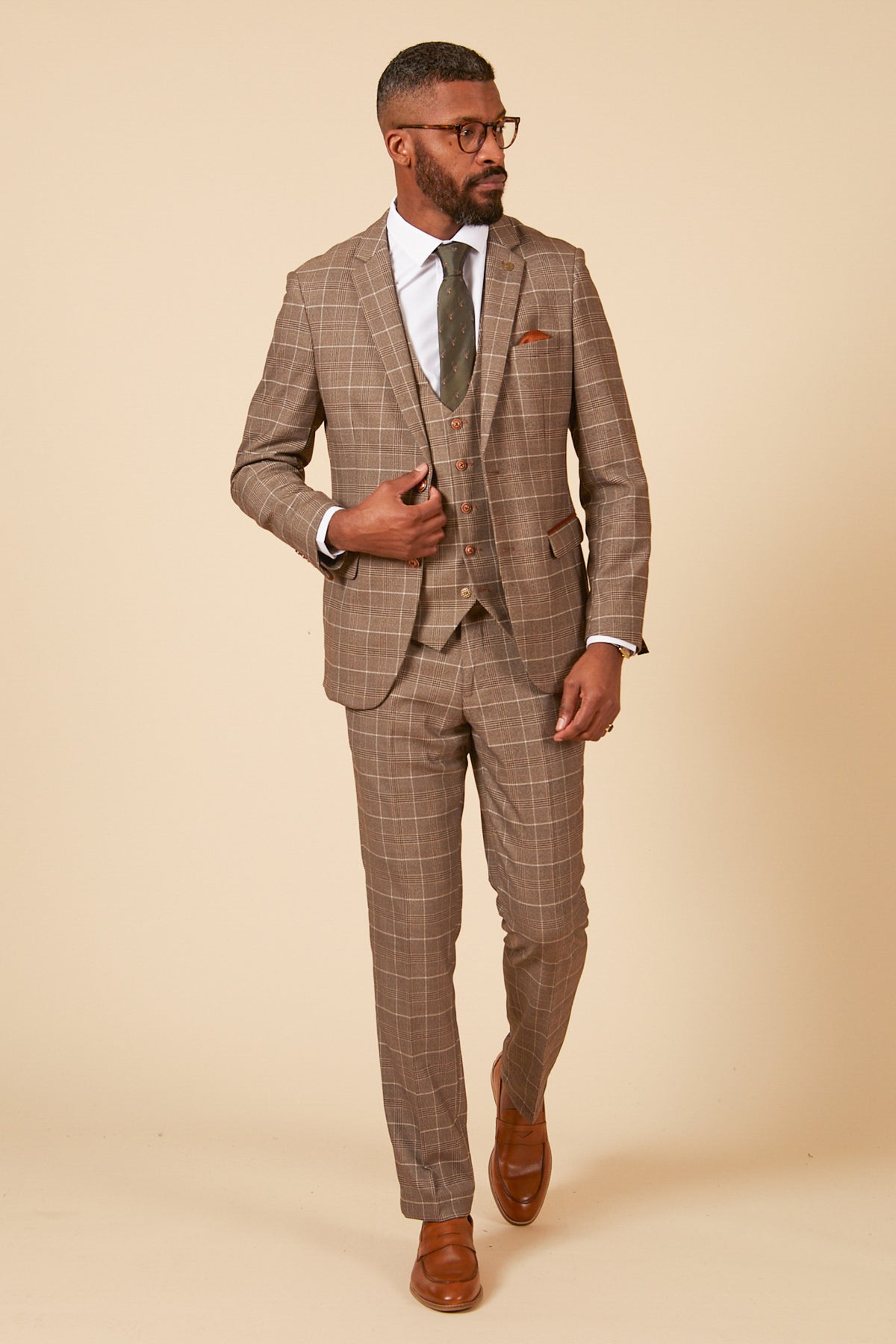 A man wearing the marcdarcy RAY Tan Check Three Piece Suit with a white shirt, green tie, and brown shoes looks to the right.