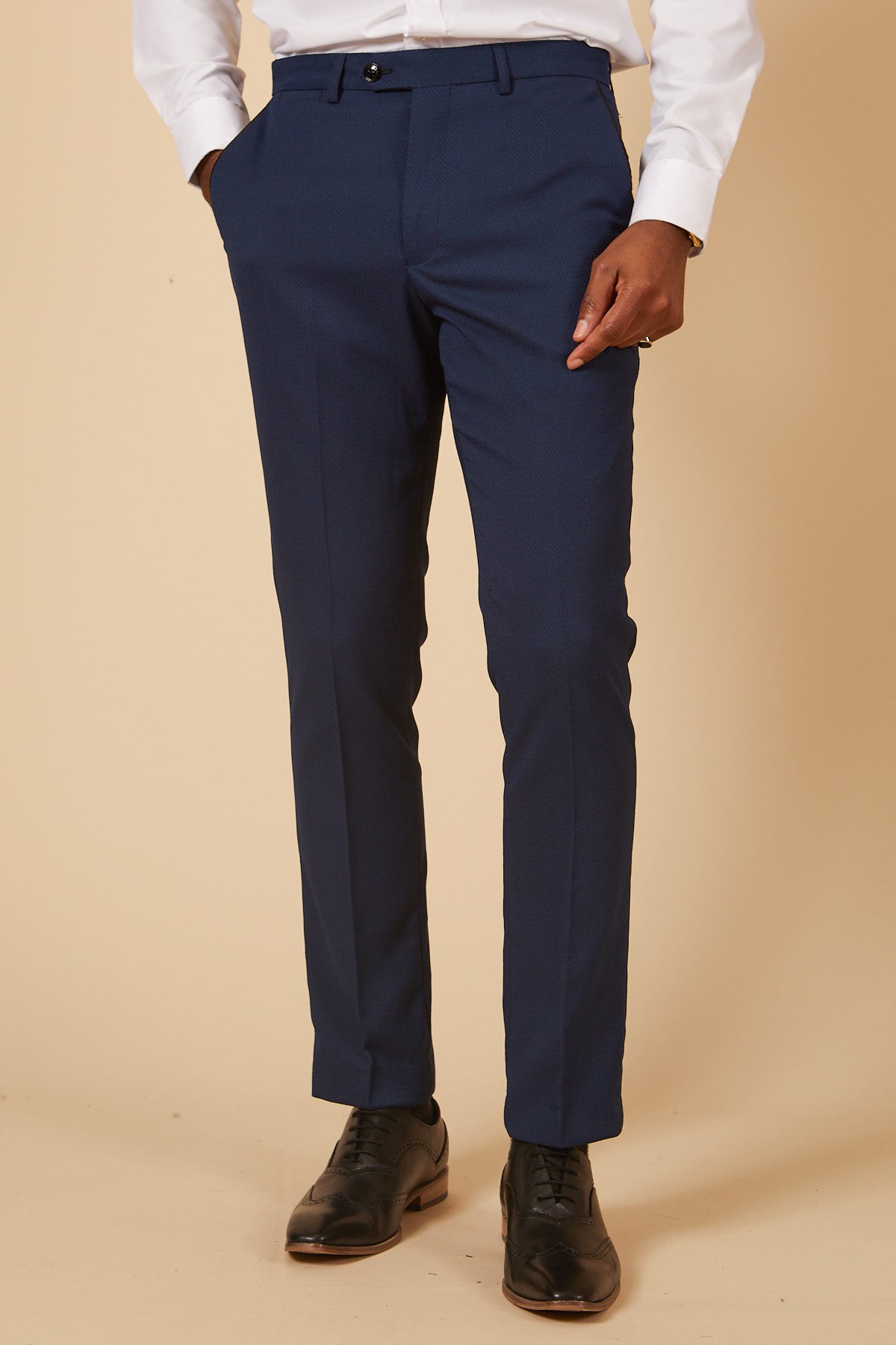 A person wearing marcdarcy DALTON - Royal Blue Diamond Trousers, a white button-down shirt, and black dress shoes stands against a beige background with hands in their pockets.