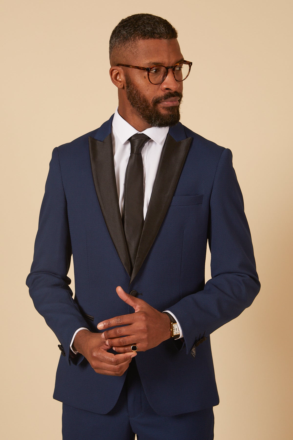 A man with short hair, a beard, and glasses models the marcdarcy DALTON - Royal Blue Tux Lapel Diamond Blazer over a white shirt and black tie, standing against a beige background—an ideal look for formal occasions.