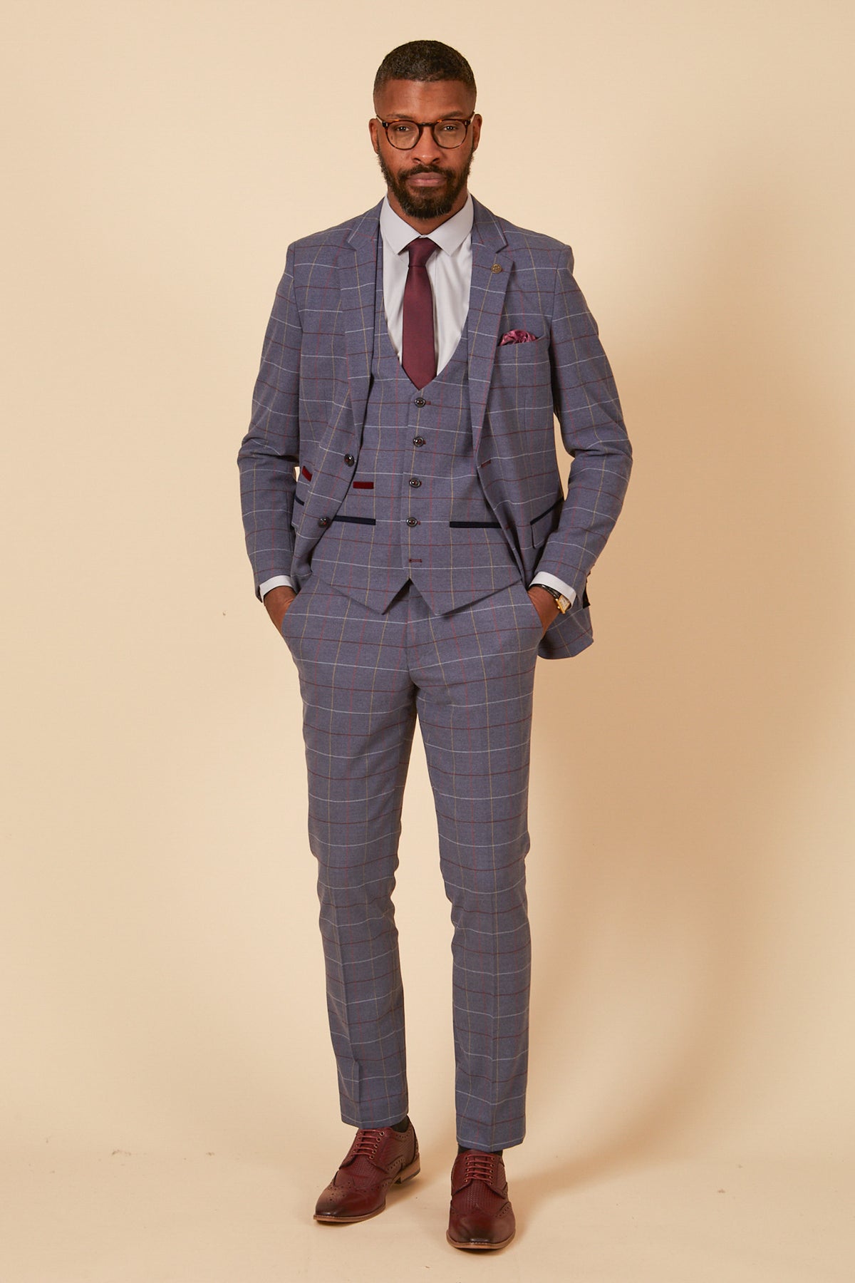 A Black man wears the marcdarcy DRAKE Sky Blue Check Three Piece Suit with a burgundy tie and pocket square, glasses, and brown dress shoes—ideal for formal occasions.