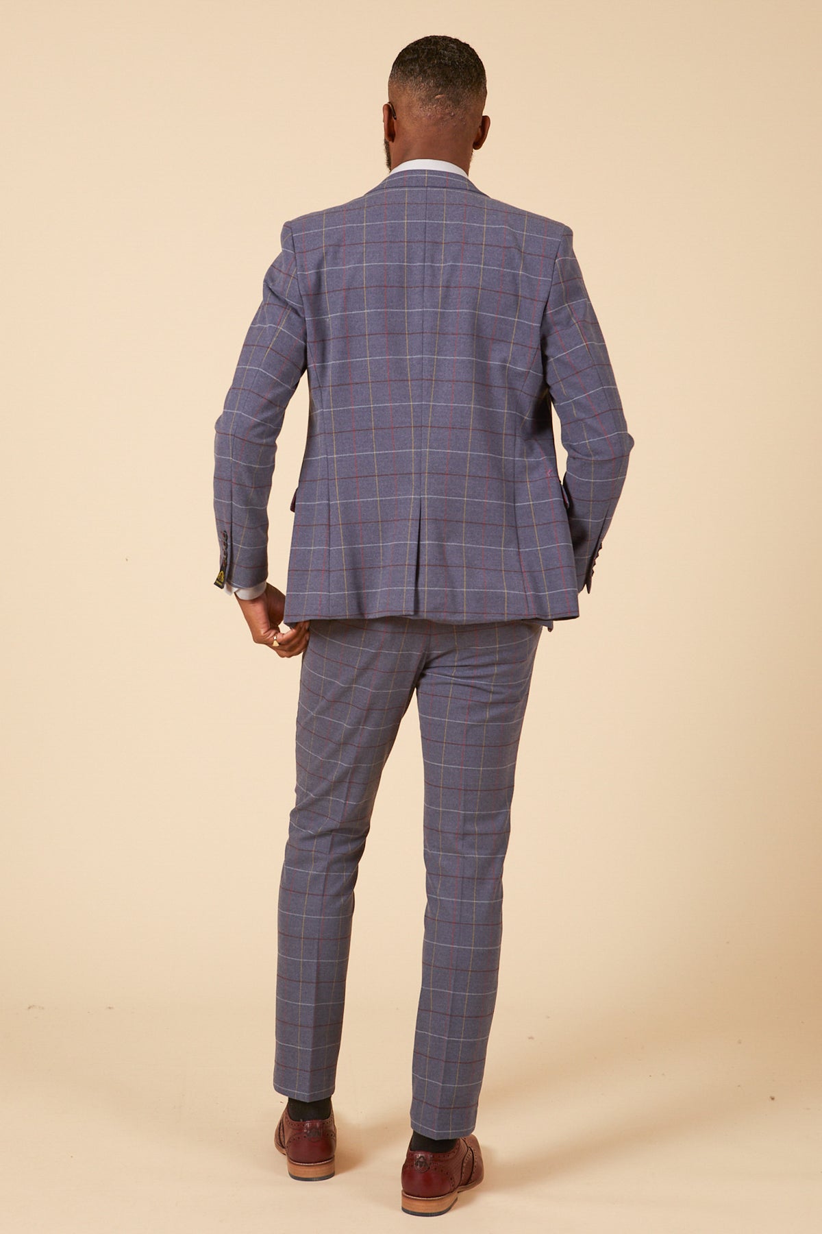 A person faces away from the camera, wearing the marcdarcy DRAKE Sky Blue Check Three Piece Suit with matching trousers and brown shoes, set against a plain beige background.