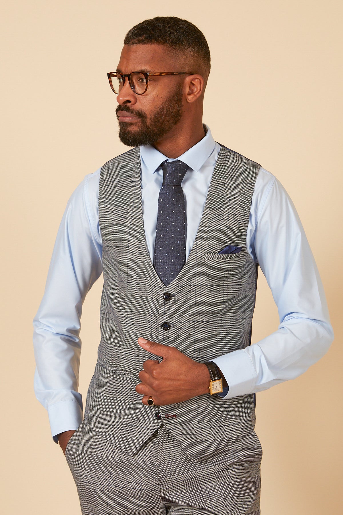 A man in a light blue shirt, tie, and glasses confidently showcases the marcdarcy JERRY Grey Check Single Breasted Waistcoat, highlighting its modern and stylish appeal.