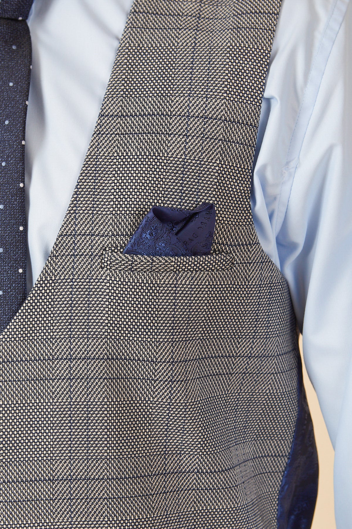 Close-up of a person in a light blue shirt, a marcdarcy JERRY Grey Check Single Breasted Waistcoat with adjuster straps, navy blue dotted tie, and a matching navy pocket square tucked into the waistcoat pocket.