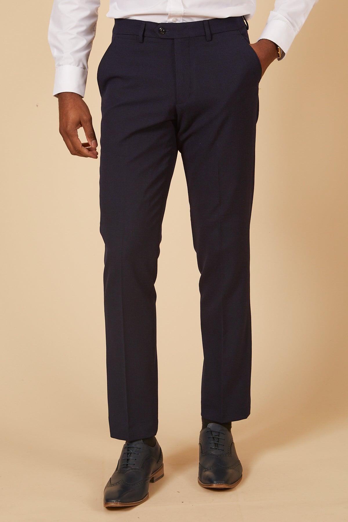 A man in the Marc Darcy "The Cardiff City F.C. Collection - BROMLEY" navy check two-piece suit as worn by Will Fish, paired with a white dress shirt and dark blue wingtip shoes, stands against a beige background.