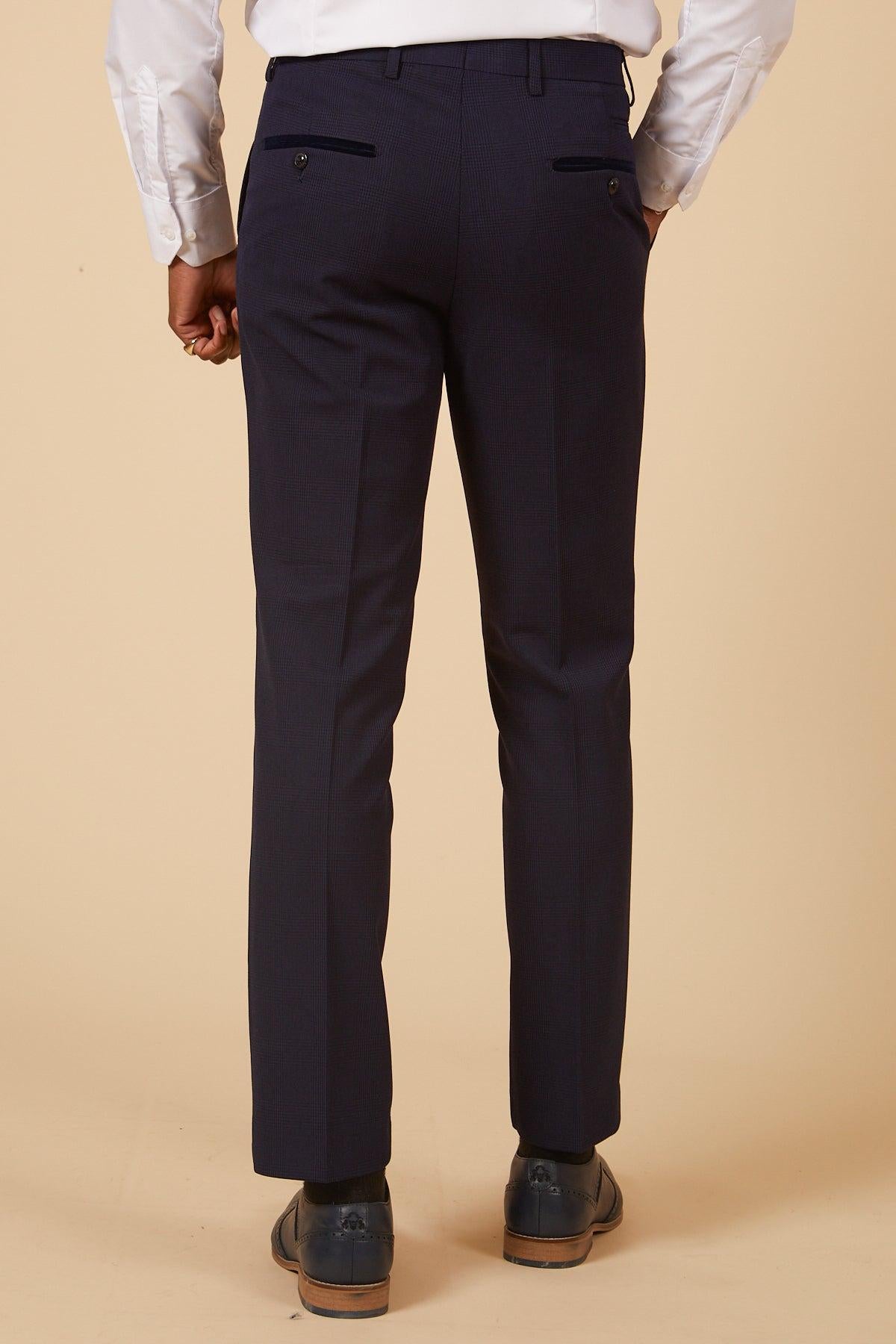 A person is seen from the back against a beige background, wearing a white shirt and Marc Darcy’s BROMLEY Navy Check Two Piece Suit from The Cardiff City F.C. Collection, as worn by Will Fish, paired with black dress shoes.