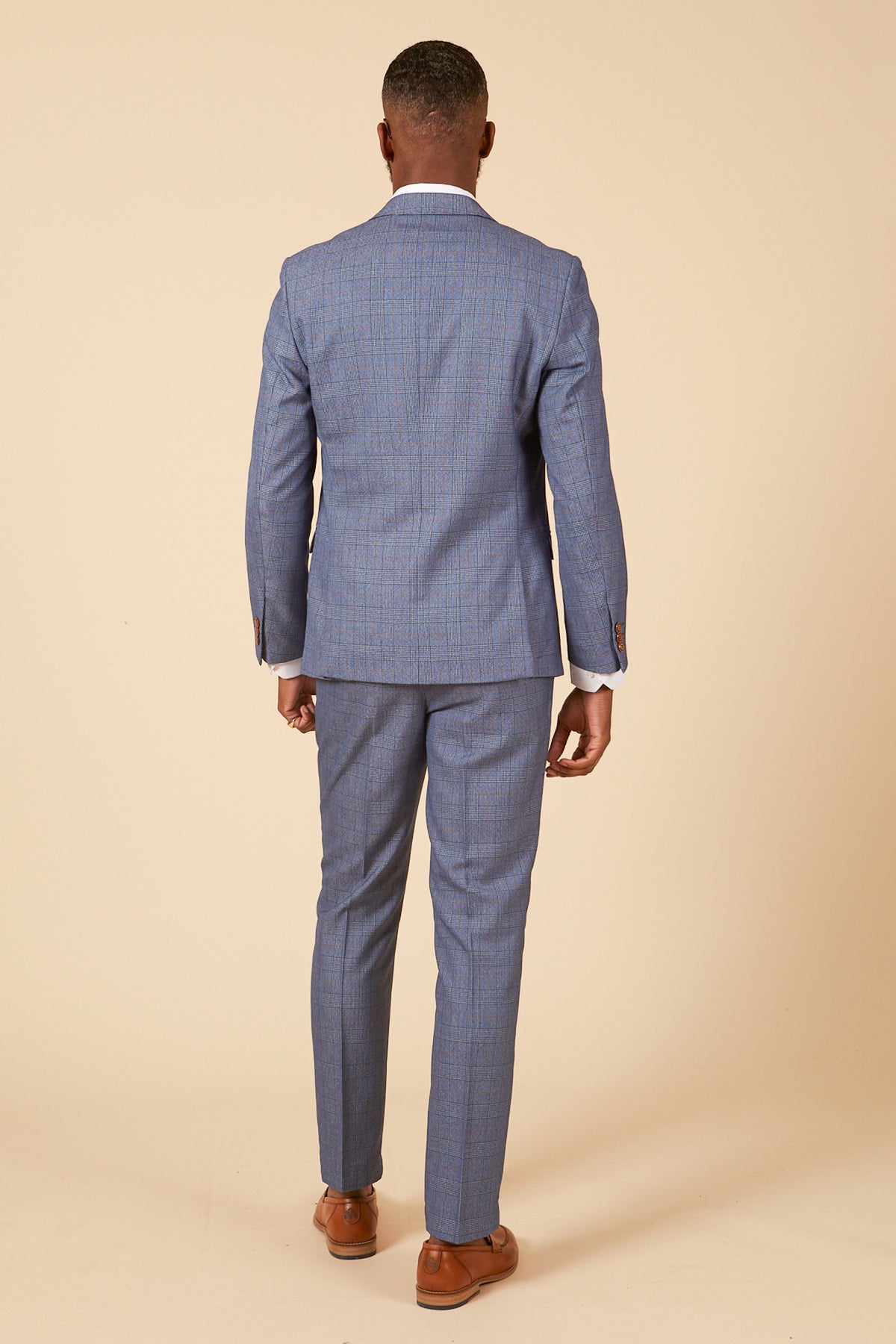 A man stands with his back to the camera wearing the marcdarcy GEORGE Light Blue Check Three Piece Suit and brown dress shoes, set against a plain beige background.