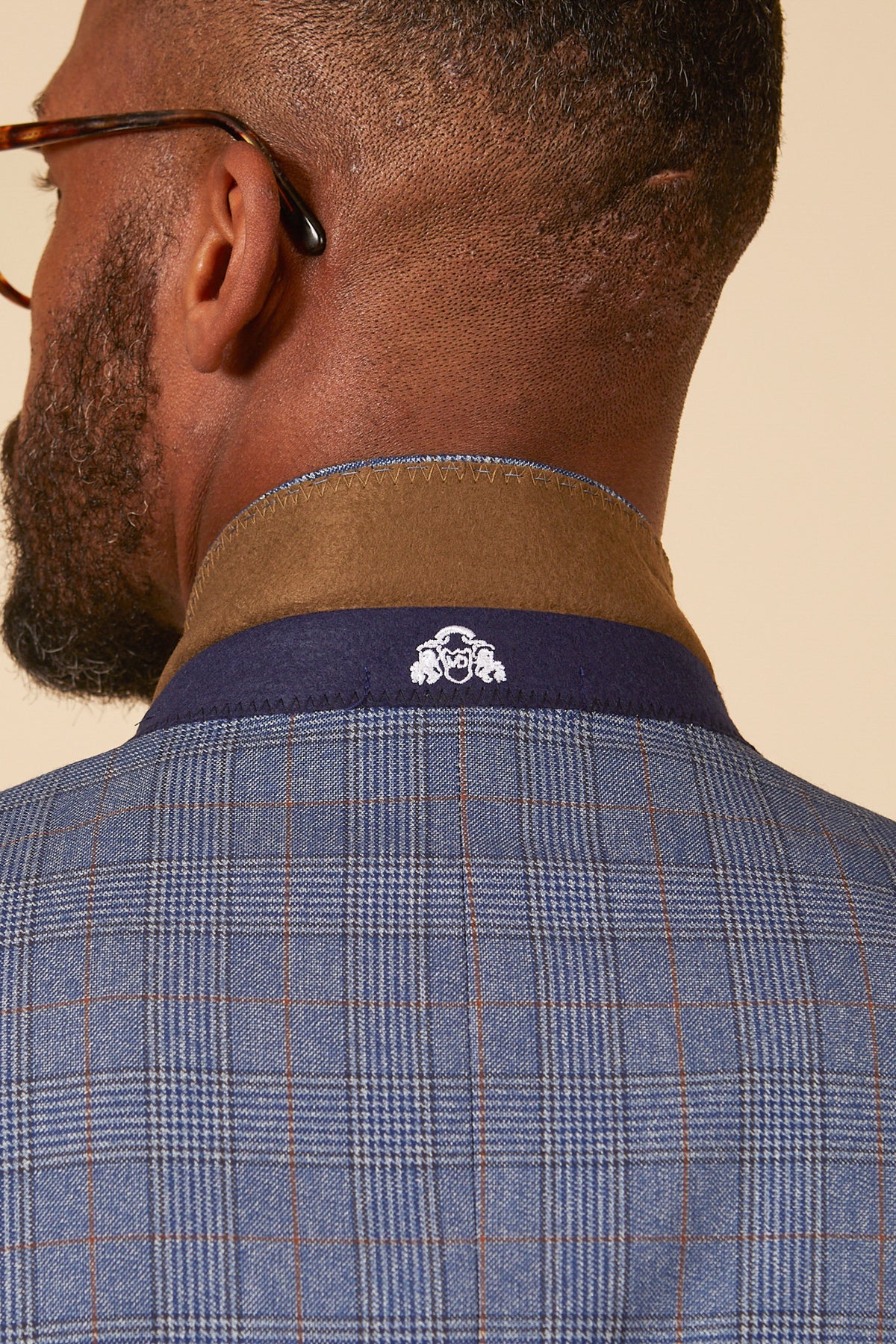 Close-up of the back of a man wearing the marcdarcy GEORGE Light Blue Check Three Piece Suit, featuring a brown collar and a white embroidered logo on the navy collar.