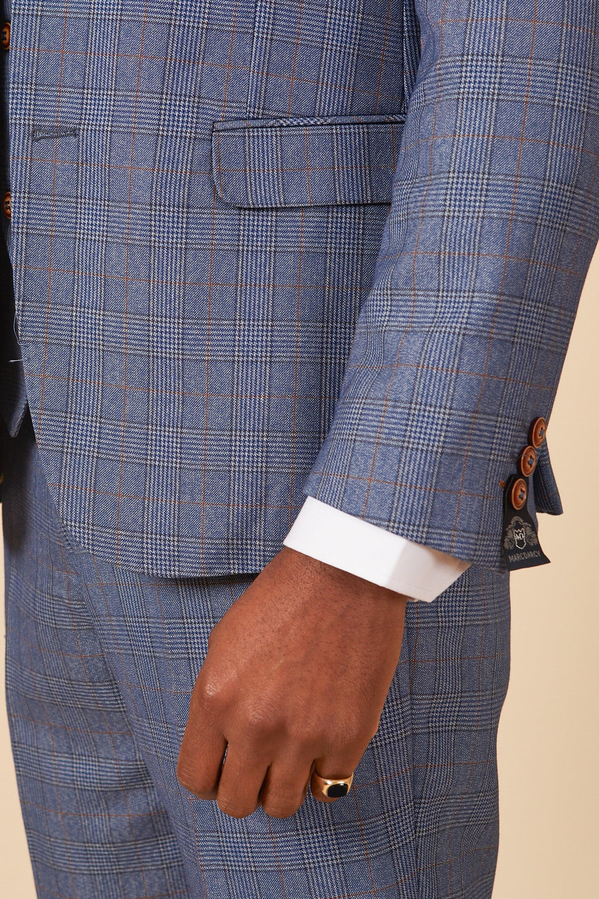 A close-up of a person wearing the marcdarcy GEORGE - Light Blue Check Three Piece Suit, featuring brown buttons, a visible white shirt cuff, a gold ring, and jacket details like a pocket and decorative cuff buttons.