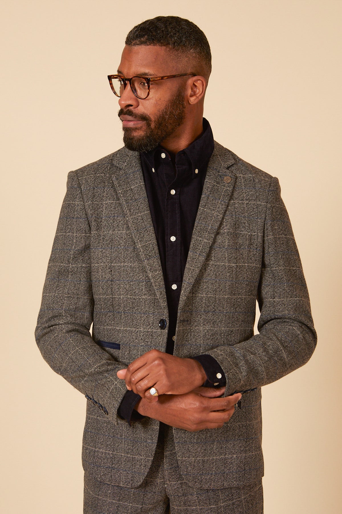 A Black man with glasses and a beard models the marcdarcy SCOTT Grey Tweed Check Blazer over a dark button-up shirt, posing against a light background.