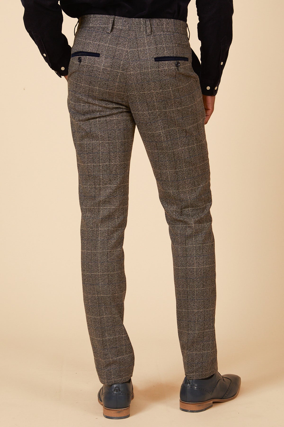 A person stands with their back to the camera against a beige background, wearing marcdarcy SCOTT Grey Check Tweed Trousers, a black shirt, and gray dress shoes.