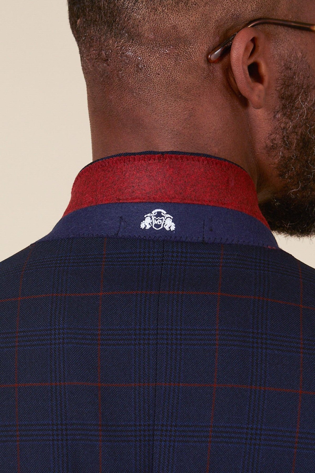 Close-up of a man's neck and shoulders wearing the Marc Darcy EDINSON - Navy Wine Check Two Piece Suit, featuring red and blue trim and an embroidered logo.