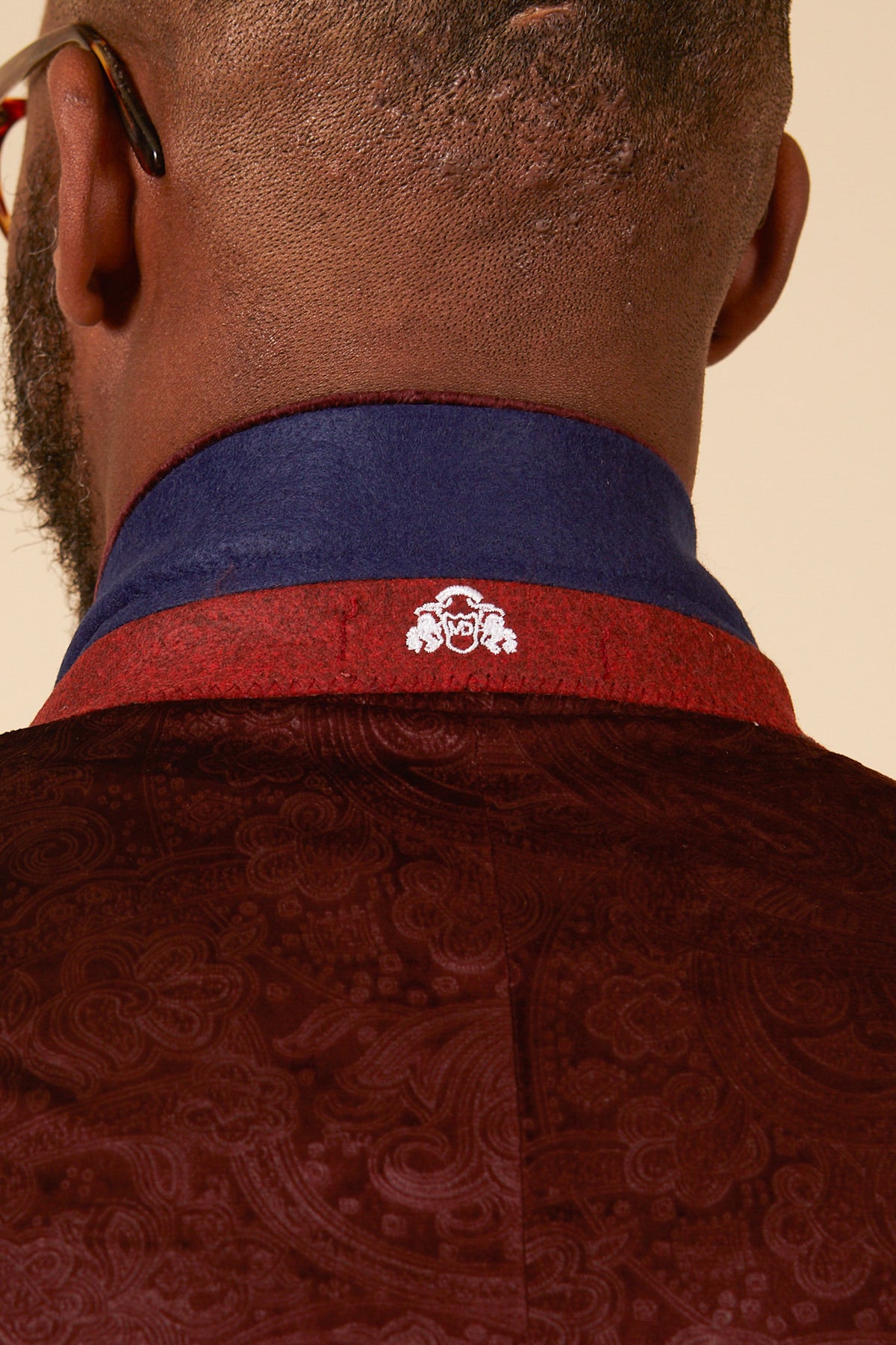 Close-up of the back of a person's neck and shoulders, wearing the Marc Darcy SIMON Wine Velvet Jacquard Three Piece Suit featuring a blue collar with a small white embroidered lion face logo.