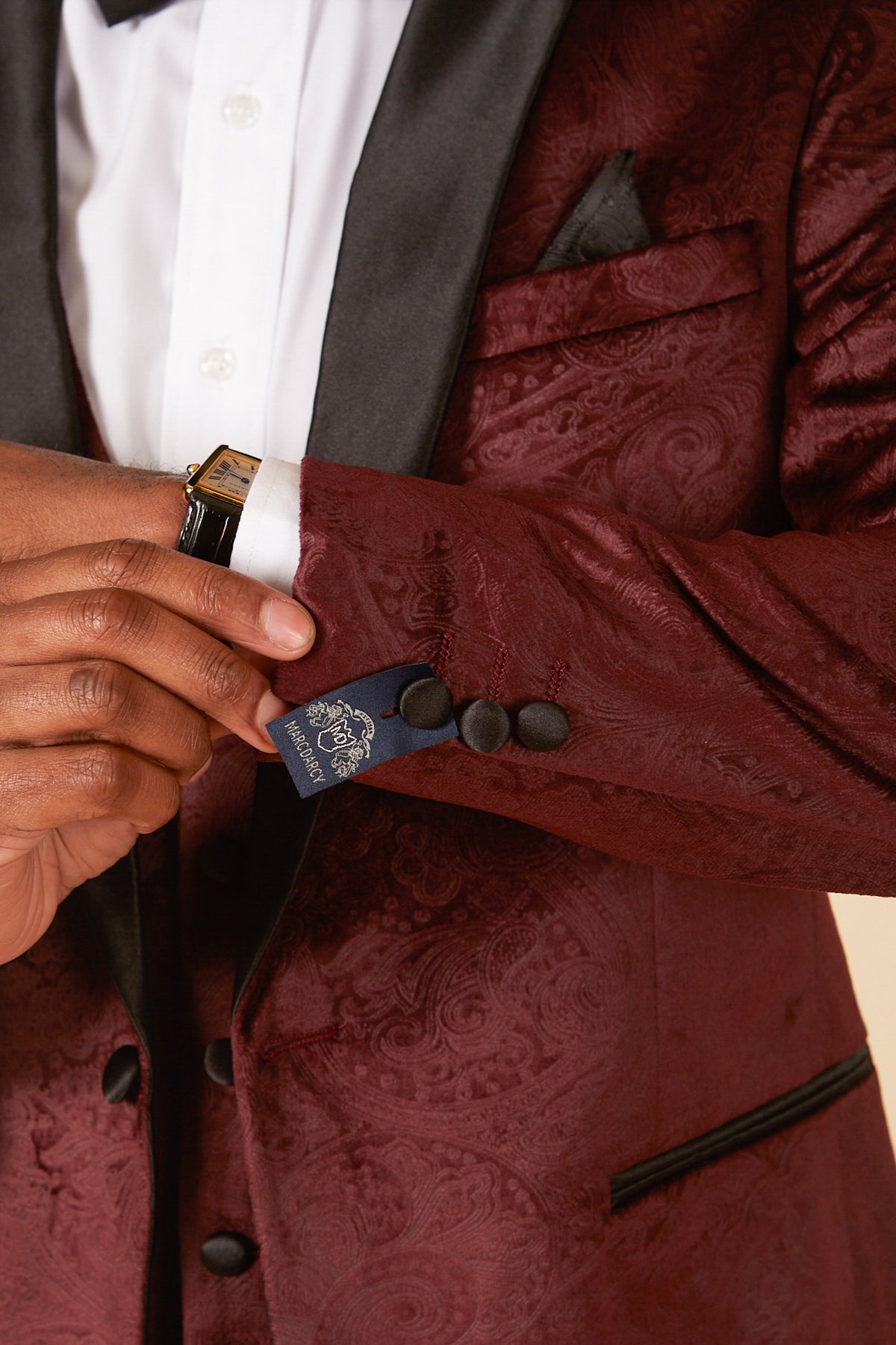 A person adjusts the cuff of the SIMON - Wine Velvet Jacquard Three Piece Suit by Marc Darcy, featuring black lapels, a white shirt, black bow tie, and a watch—an ideal choice for stylish party wear.