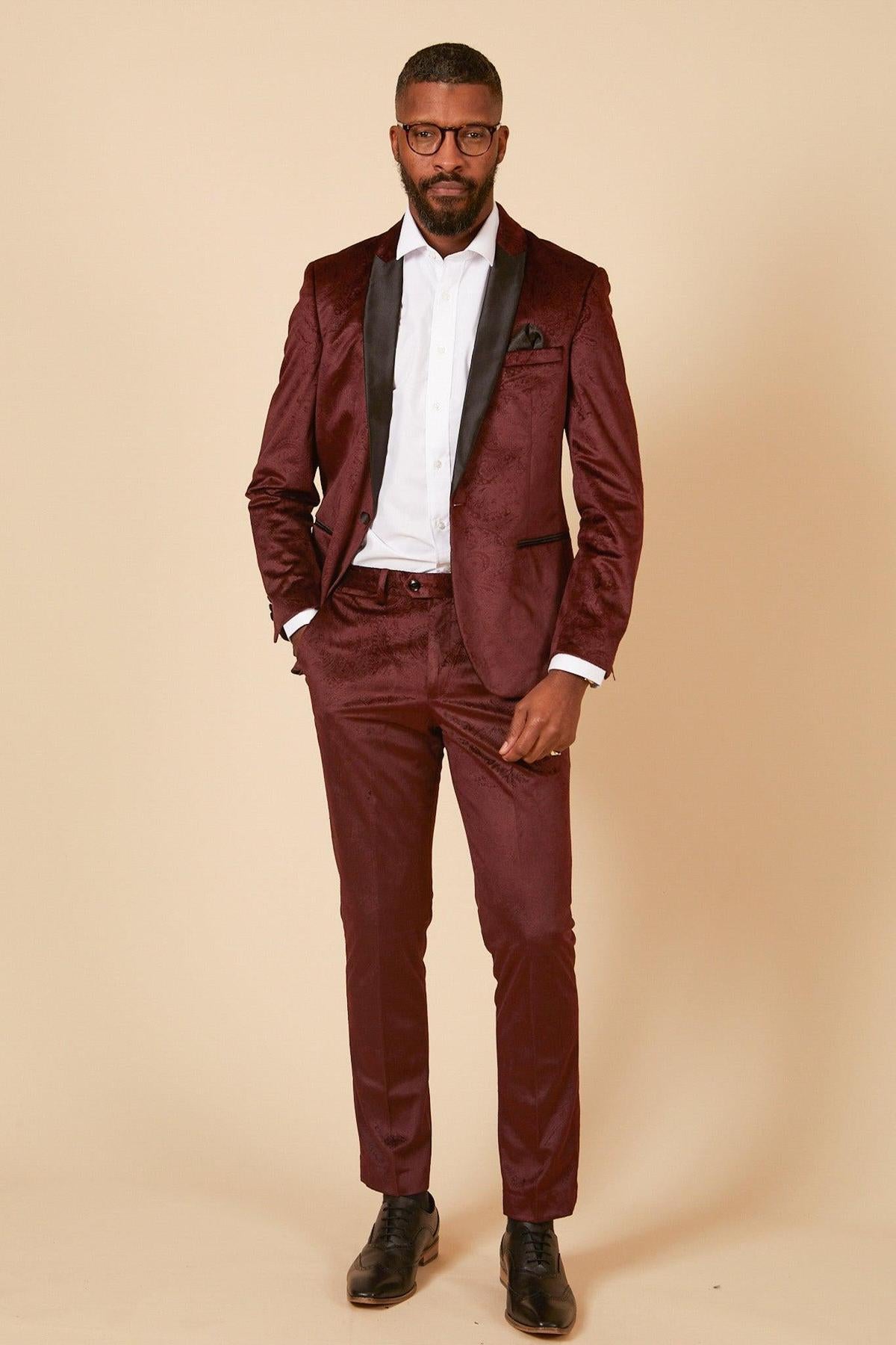 A man with short hair, a beard, and glasses stands against a beige background wearing the marcdarcy SIMON - Velvet Wine Tux Lapel Jacquard Blazer, paired with a white dress shirt and black dress shoes.
