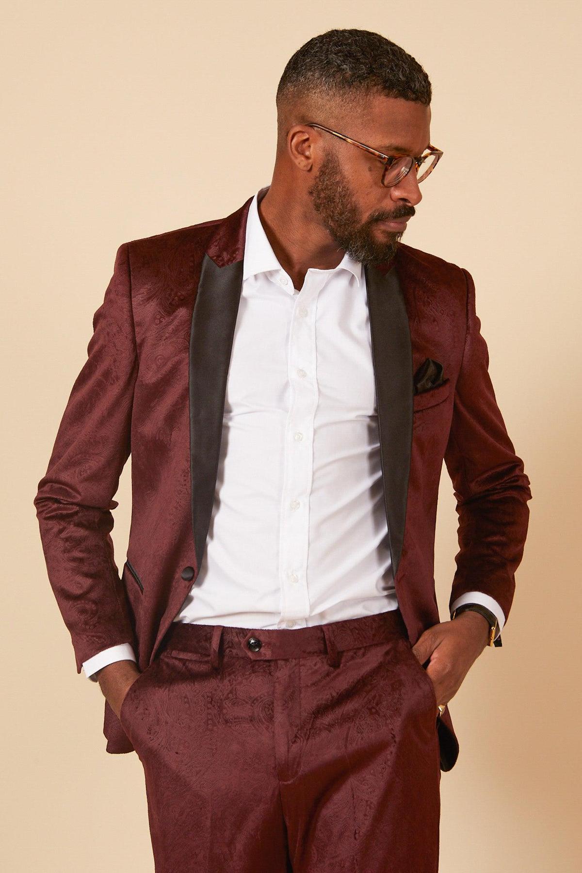 A man with short hair and a beard wears glasses, a white shirt, and the marcdarcy SIMON - Velvet Wine Tux Lapel Jacquard Blazer. He stands with hands in pockets, looking to the side against a beige background.