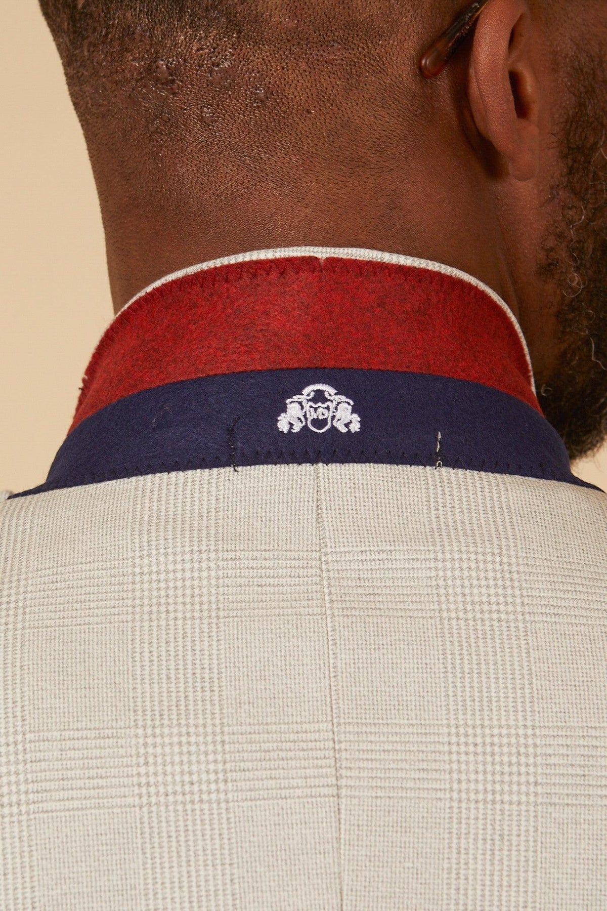 Close-up of the back of Fabian Delph’s neck wearing the Marc Darcy BROMLEY Stone Check Suit, featuring a Prince of Wales pattern and a red and navy-collared detail with a small white embroidered emblem at the center.