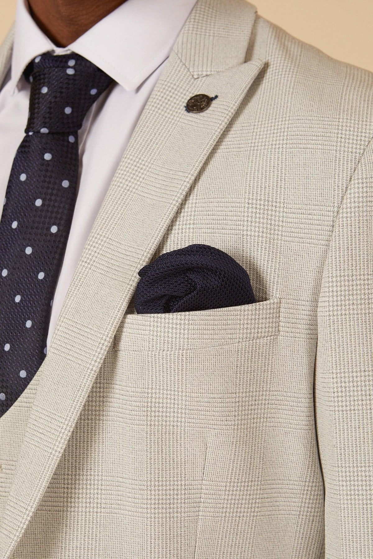 Close-up of former Manchester City footballer Fabian Delph in the Marc Darcy BROMLEY Stone Check Suit—light beige Prince of Wales check jacket, white dress shirt, navy polka dot tie, and navy pocket square.