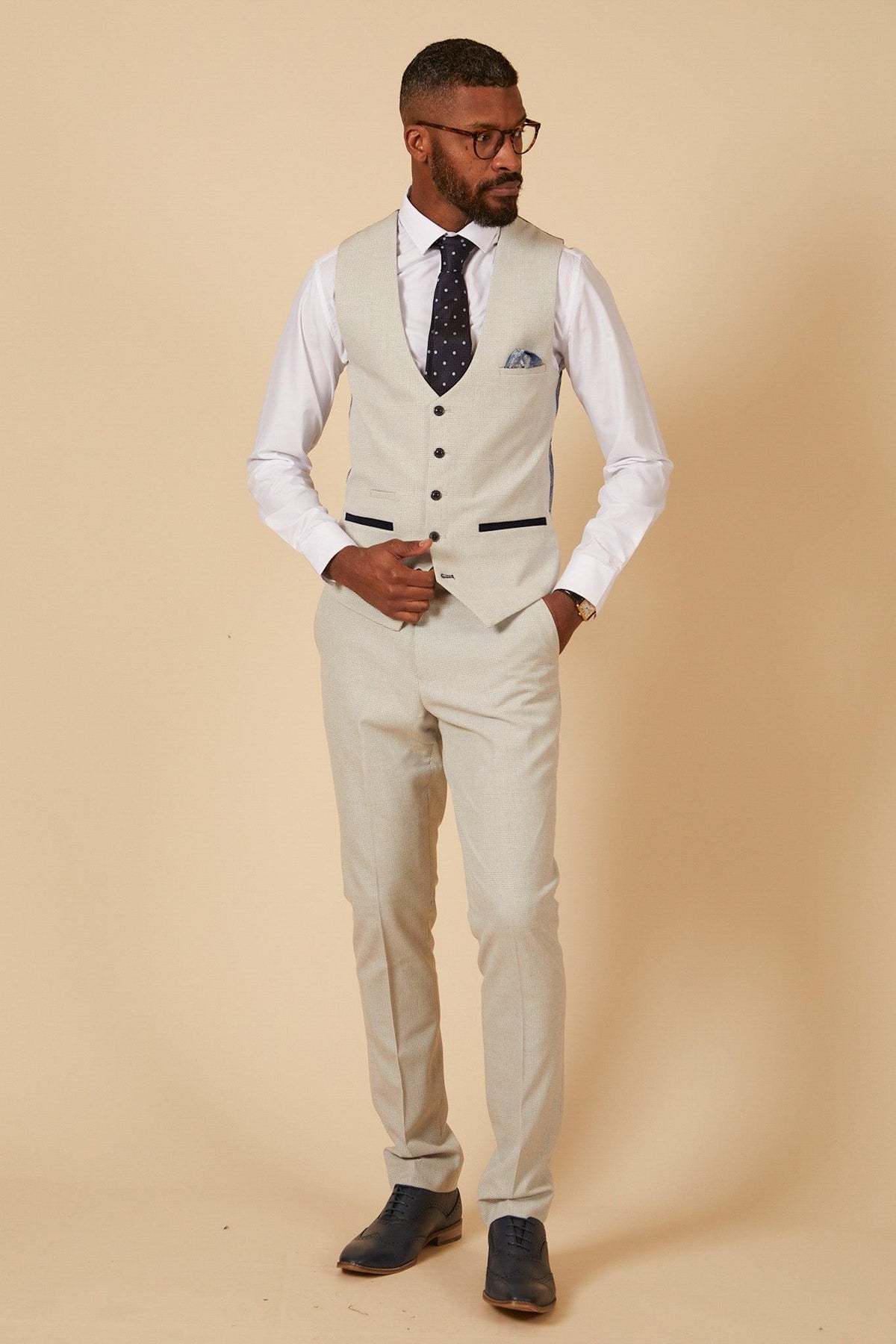 Former Manchester City footballer Fabian Delph wears the Marc Darcy BROMLEY Stone Check Suit, showcasing modern elegance with a white shirt, dark dotted tie, glasses, pocket square, and dark shoes.