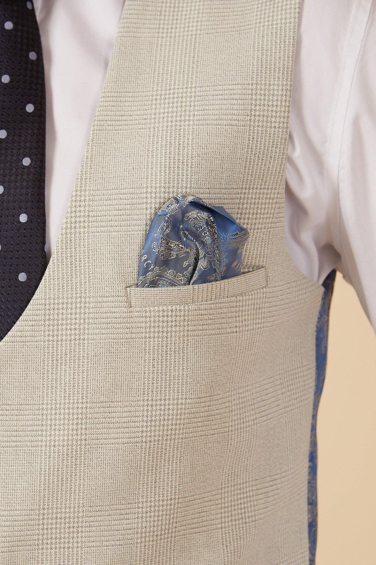 A close-up of former Manchester City footballer Fabian Delph in a Marc Darcy BROMLEY Stone Check Suit, featuring a light plaid vest, white shirt, navy polka dot tie, and blue paisley pocket square neatly tucked into the vest’s breast pocket.