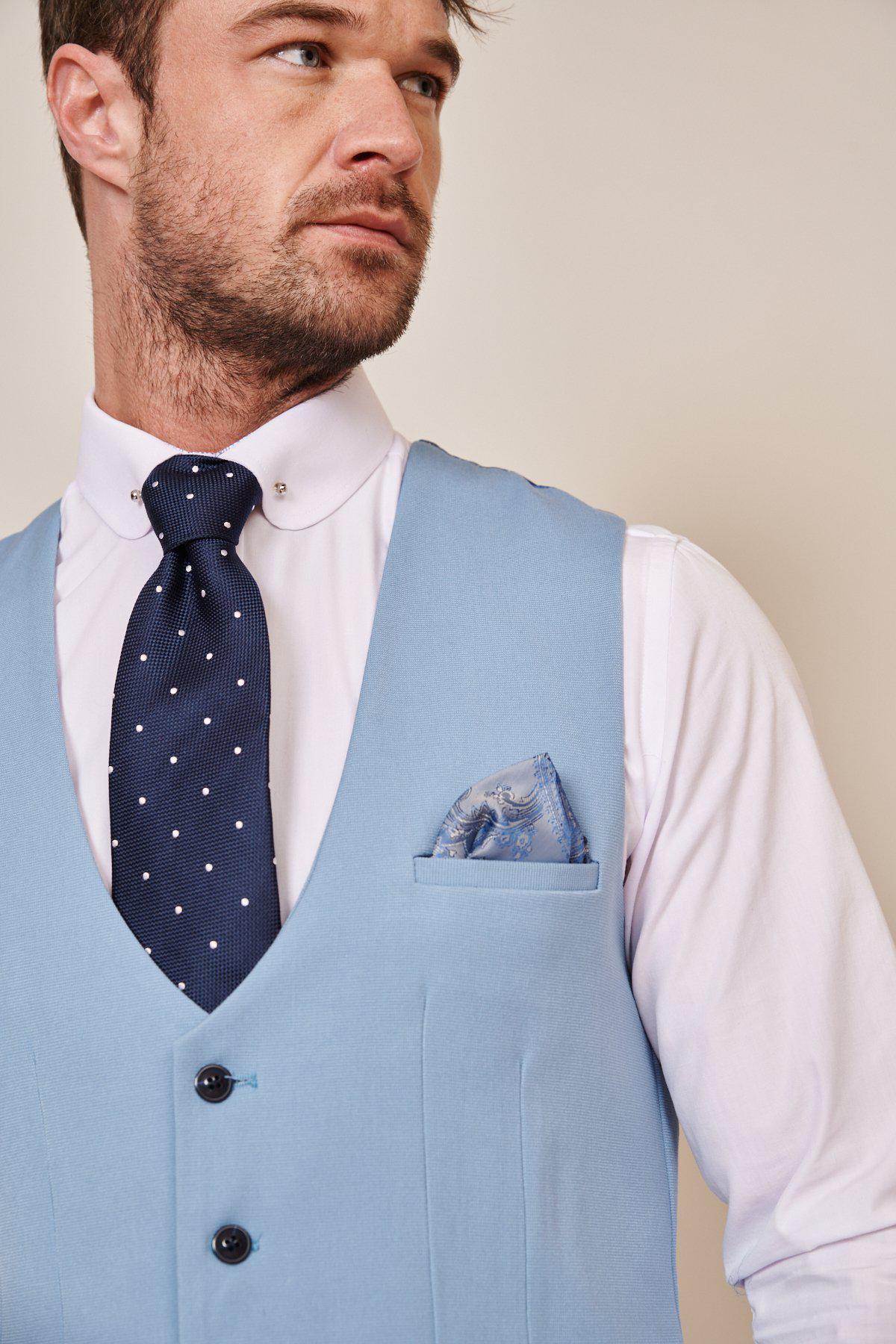A man in the marcdarcy KELLY Sky Blue Single Breasted Waistcoat pairs it with a white shirt, navy polka dot tie, and matching blue patterned pocket square, looking to the side.
