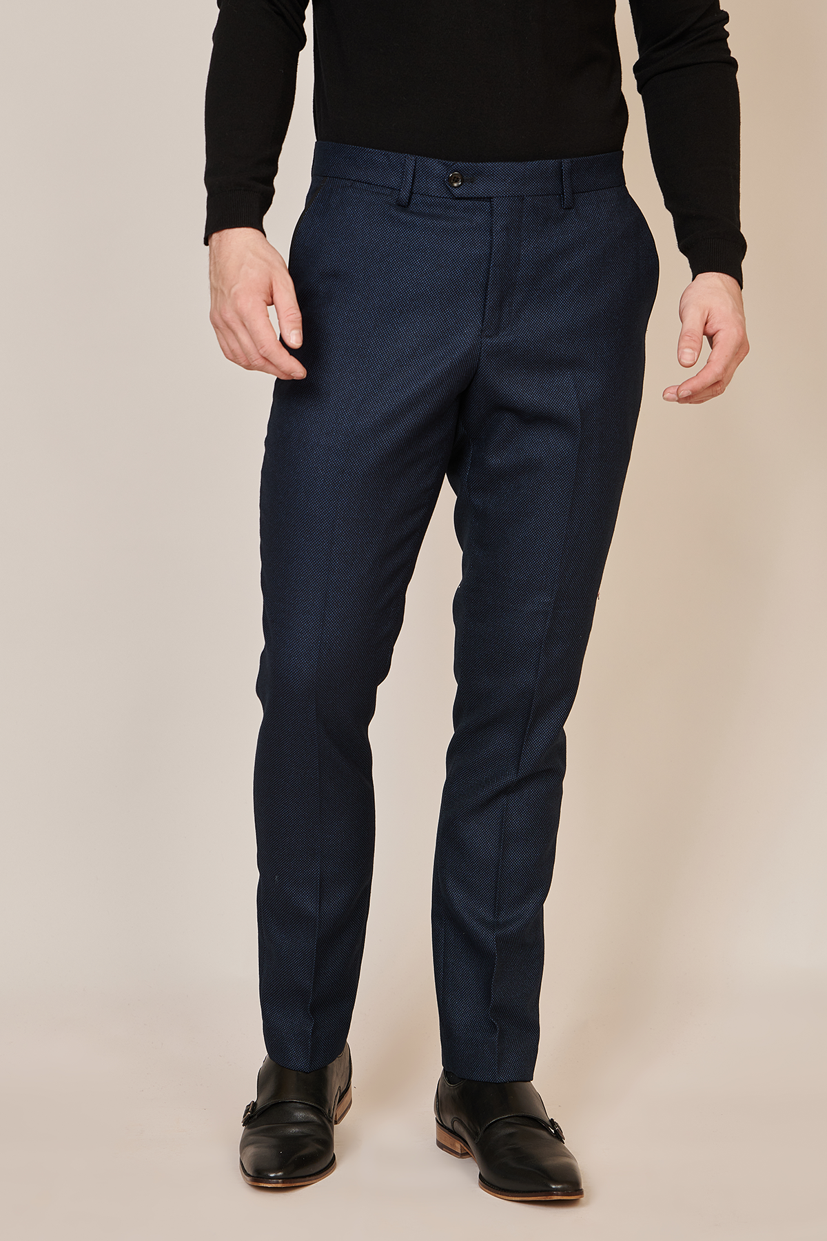 A person wearing marcdarcy CALLUM Navy Blue Trousers, a black long-sleeve shirt, and black dress shoes stands against a neutral background with arms relaxed, showcasing a smart formal look.