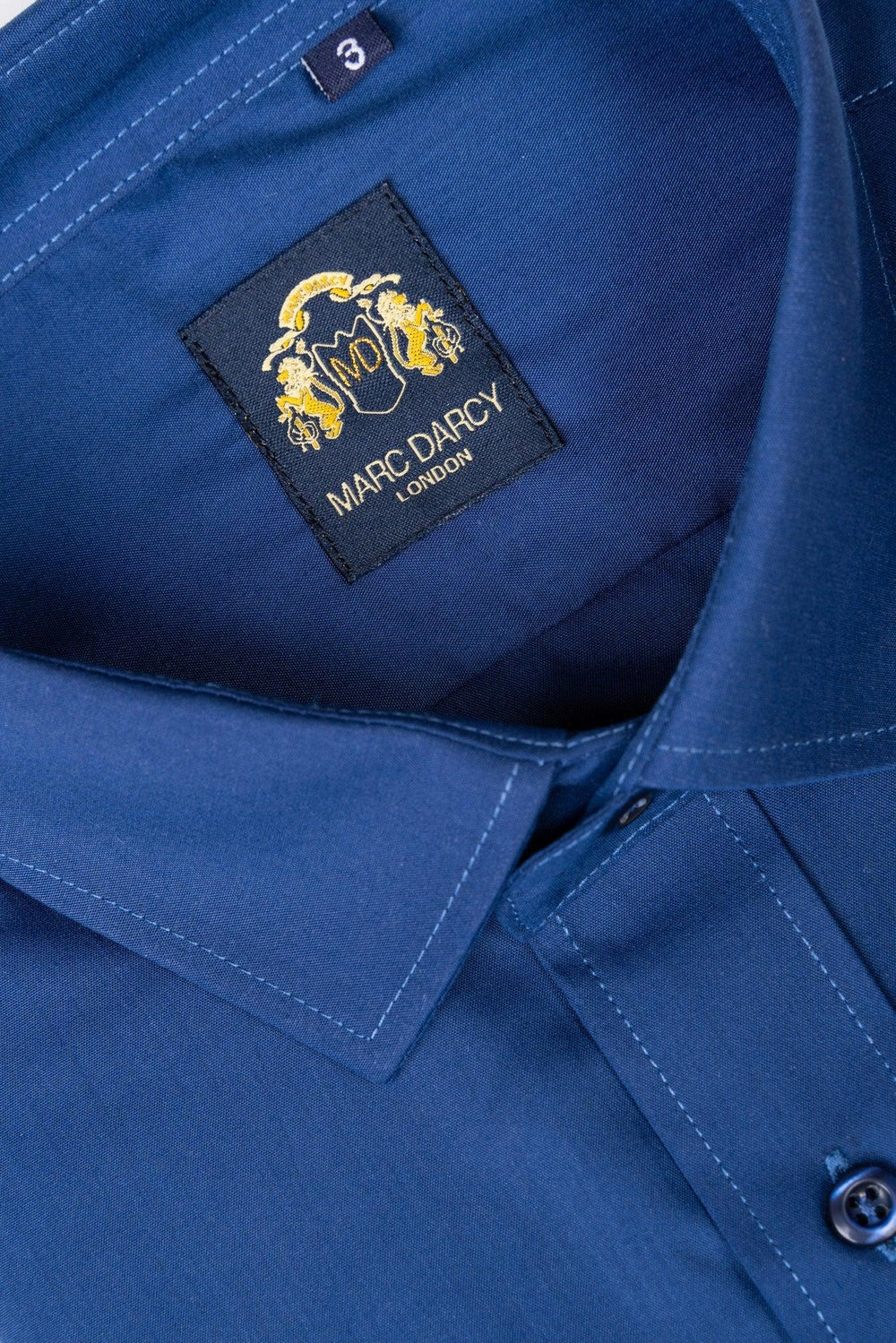 Close-up of the CARTER - Navy Long Sleeve Shirt by Marc Darcy, highlighting its collar, buttons, stitching, and inner label featuring a gold crest and the Marc Darcy brand name.