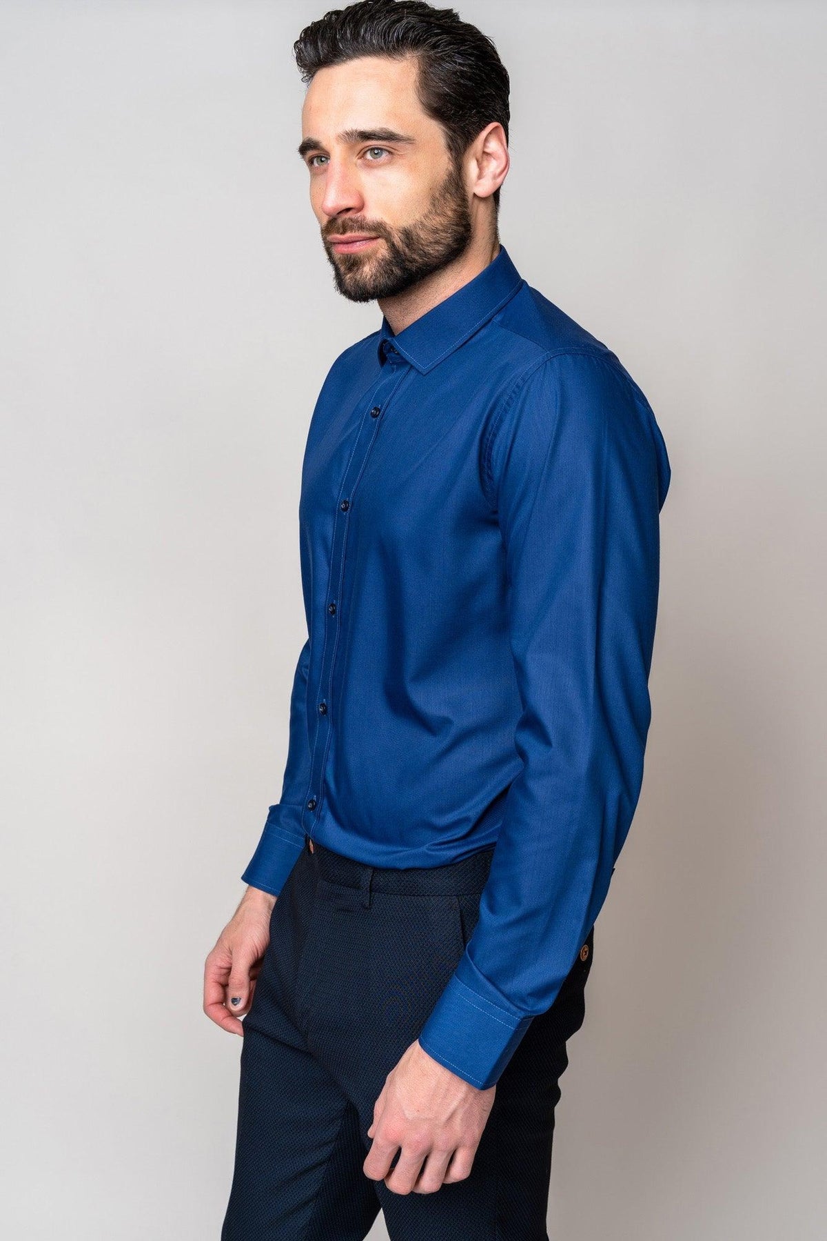 A man with dark hair and a beard wears the Marc Darcy CARTER Navy Long Sleeve Shirt with a spread collar and dark pants. He stands against a plain light background, looking slightly to the side.