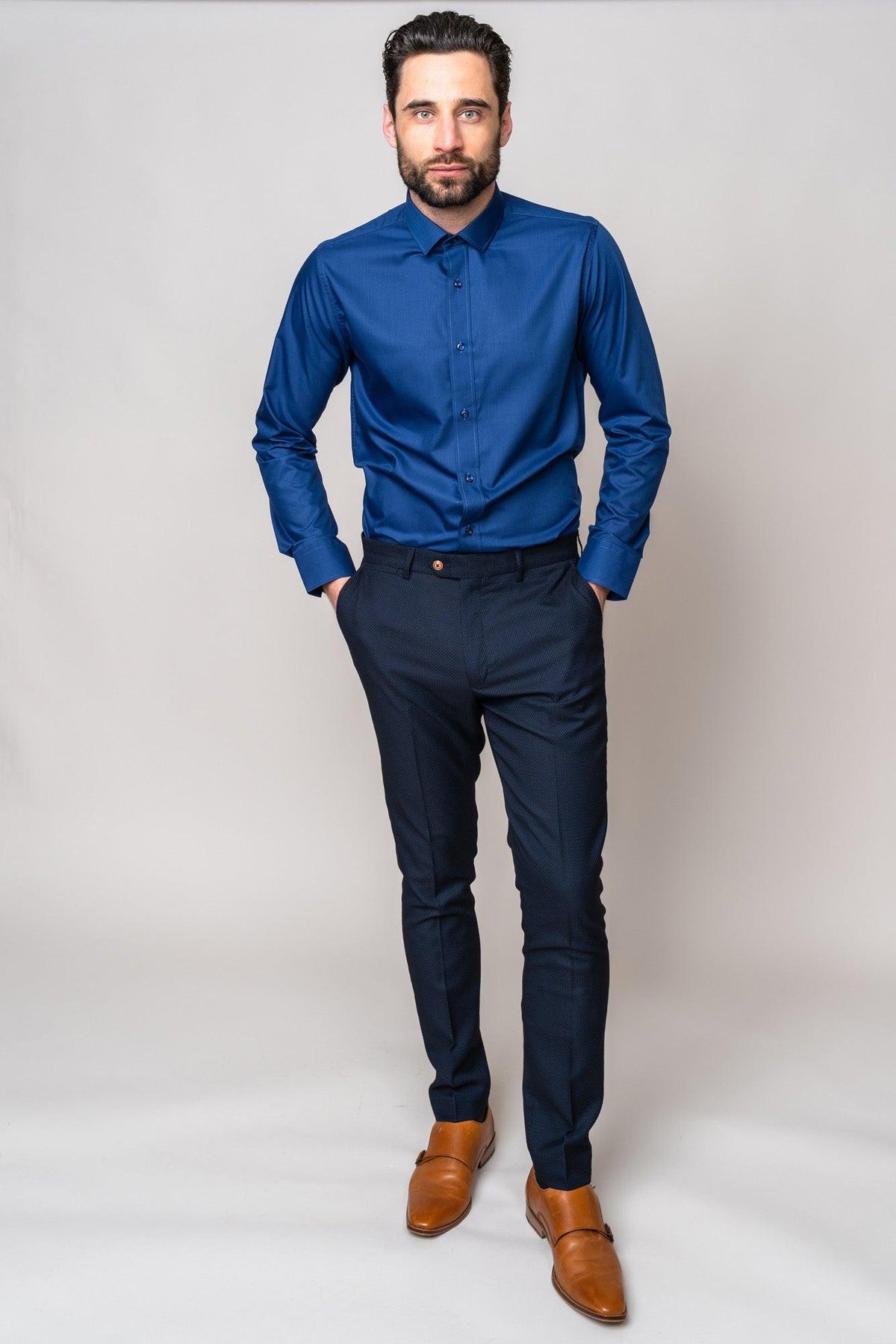 A man with dark hair and a beard wears a Marc Darcy CARTER navy long sleeve shirt, navy pinstripe pants, and brown loafers. He stands with his hands in his pockets.